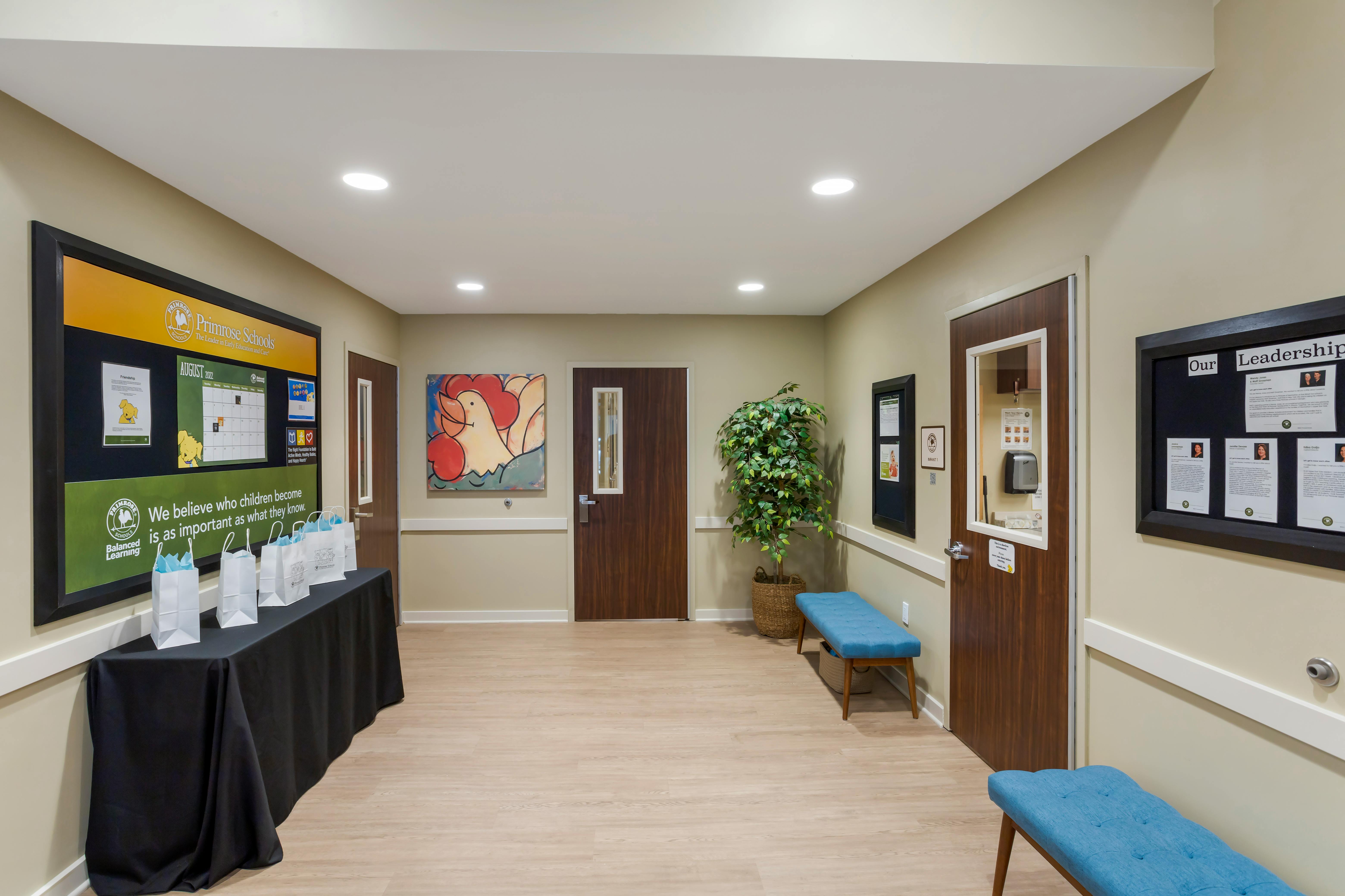 Hallway with three doors, a display board, a table with gift bags, and benches