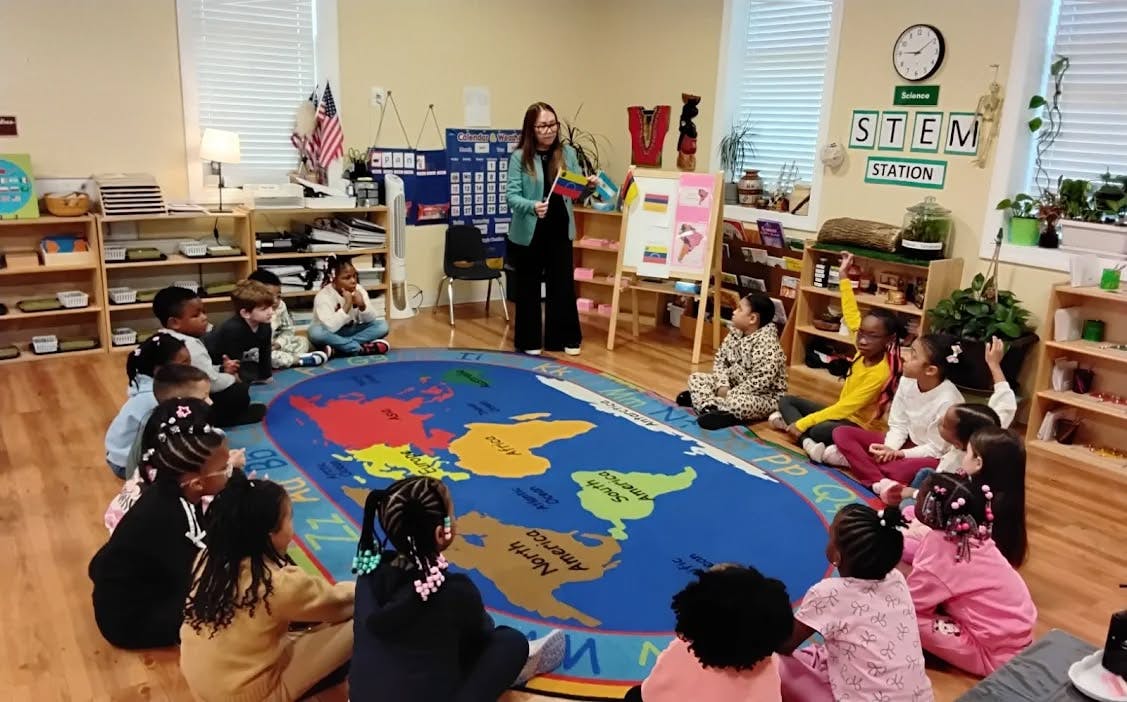 adult showing flags to children sitting on a map rug in a classroom