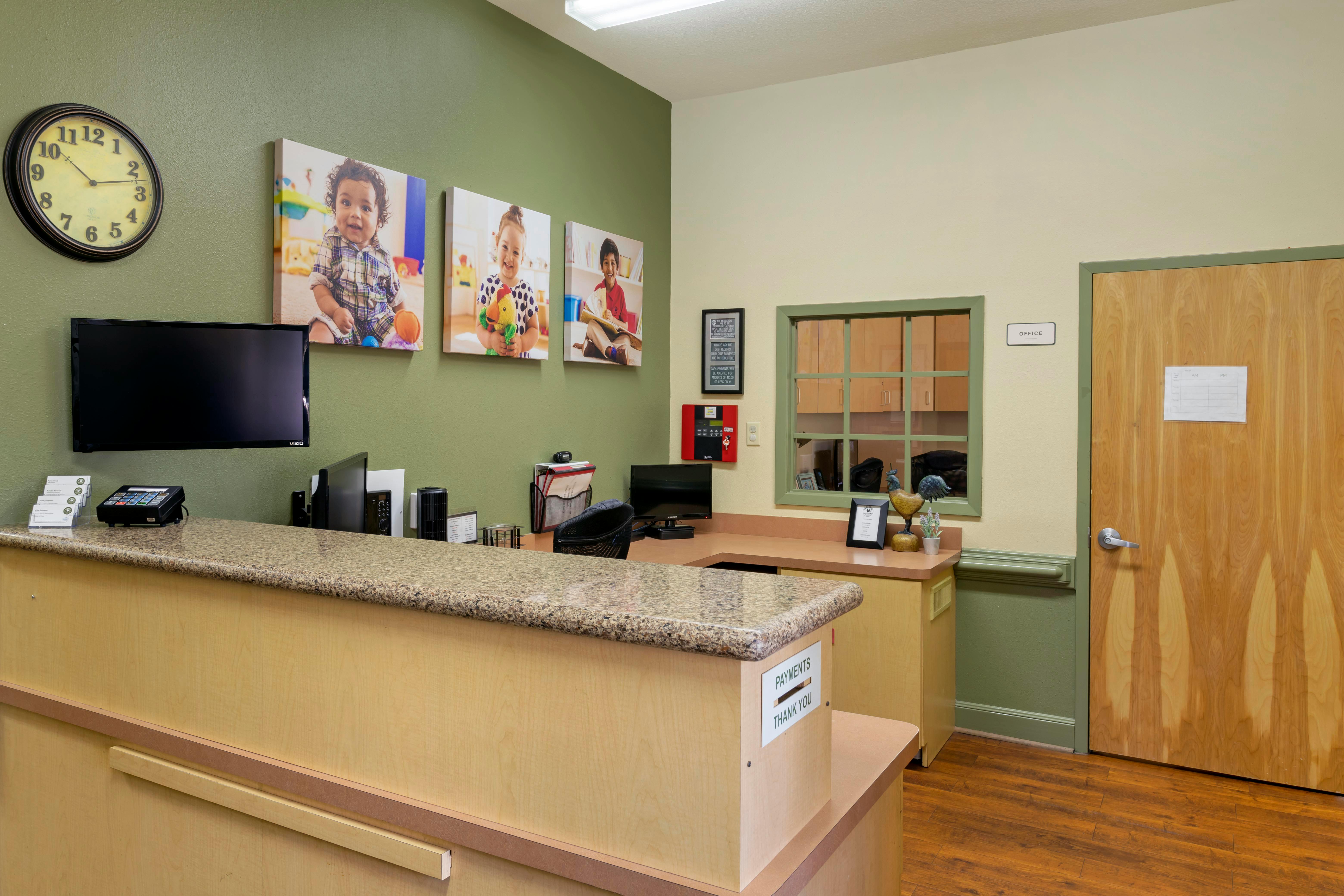 Reception desk with three framed images of children and a wall clock