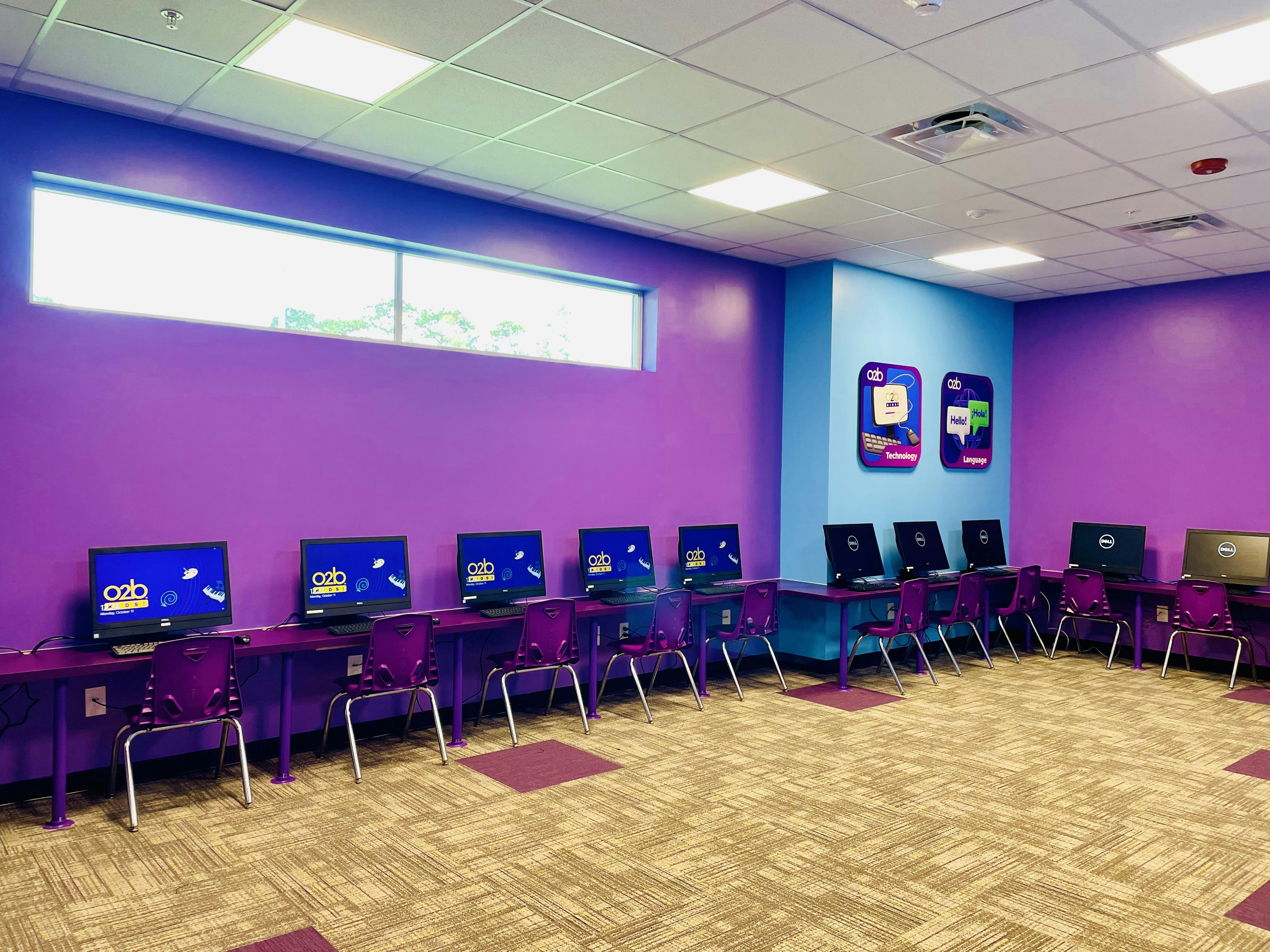 A computer lab with rows of monitors on purple desks and matching chairs