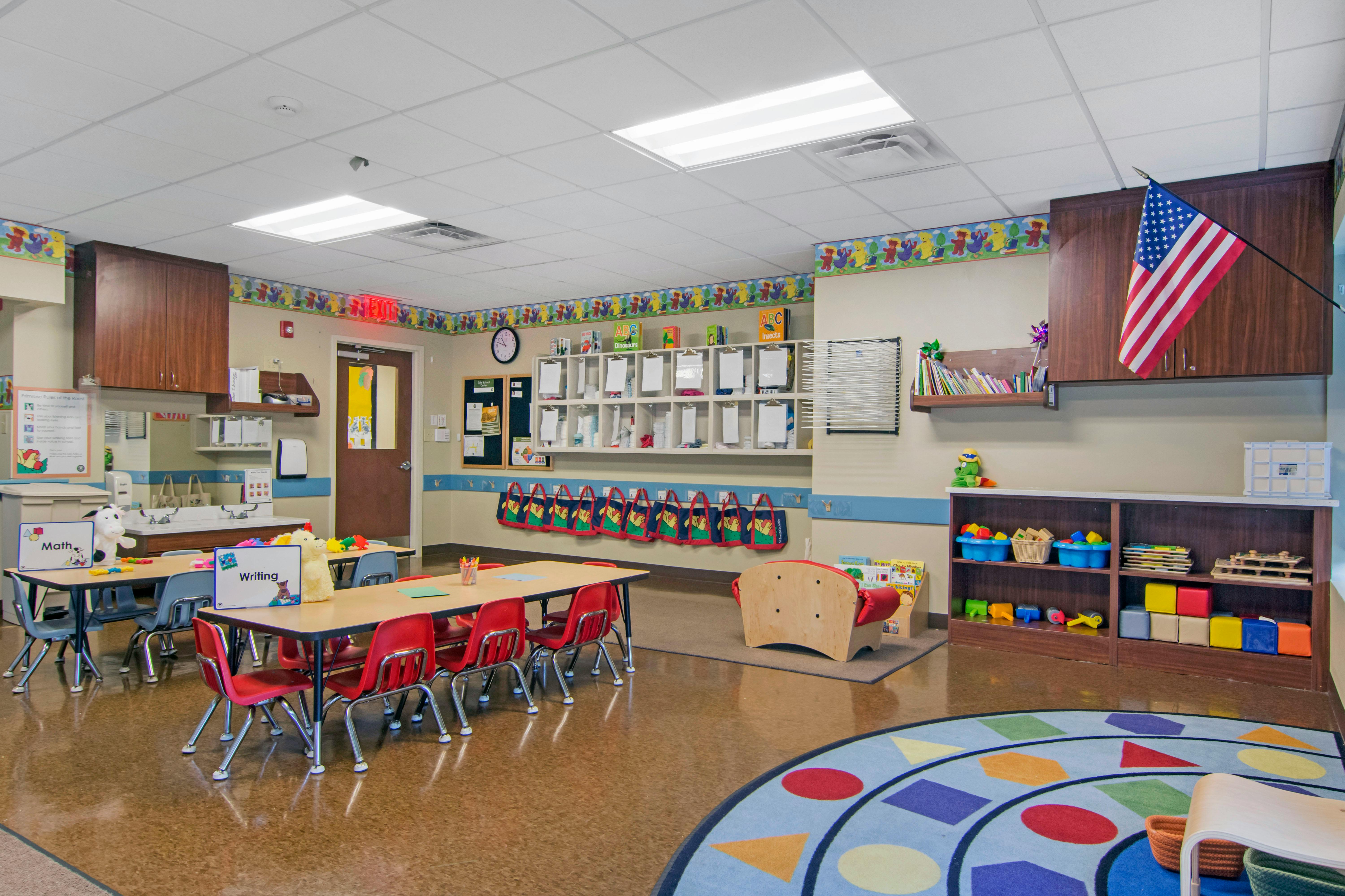 Classroom with small tables and chairs, a sink area, and toy shelves