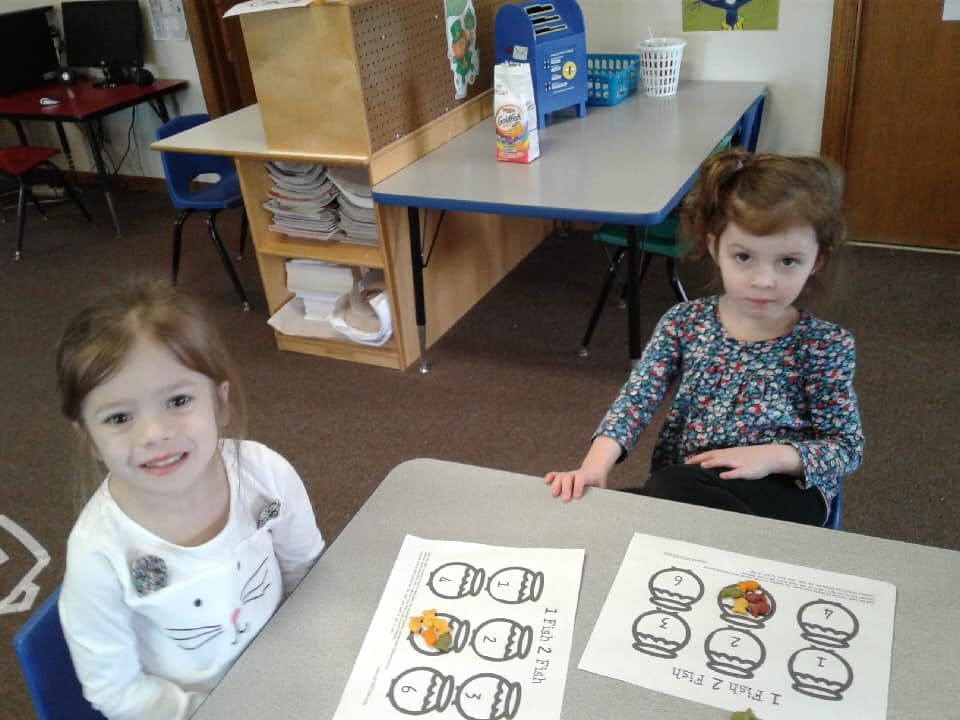 Two children sitting at a table with papers in-progress coloring pages