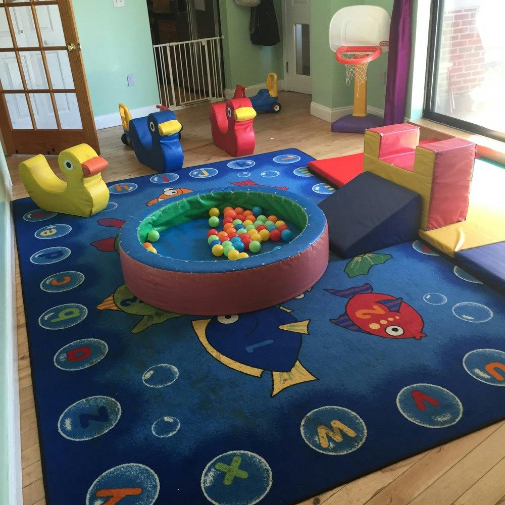 Playroom with a ball pit, soft play blocks, and ride-on toys on a blue rug