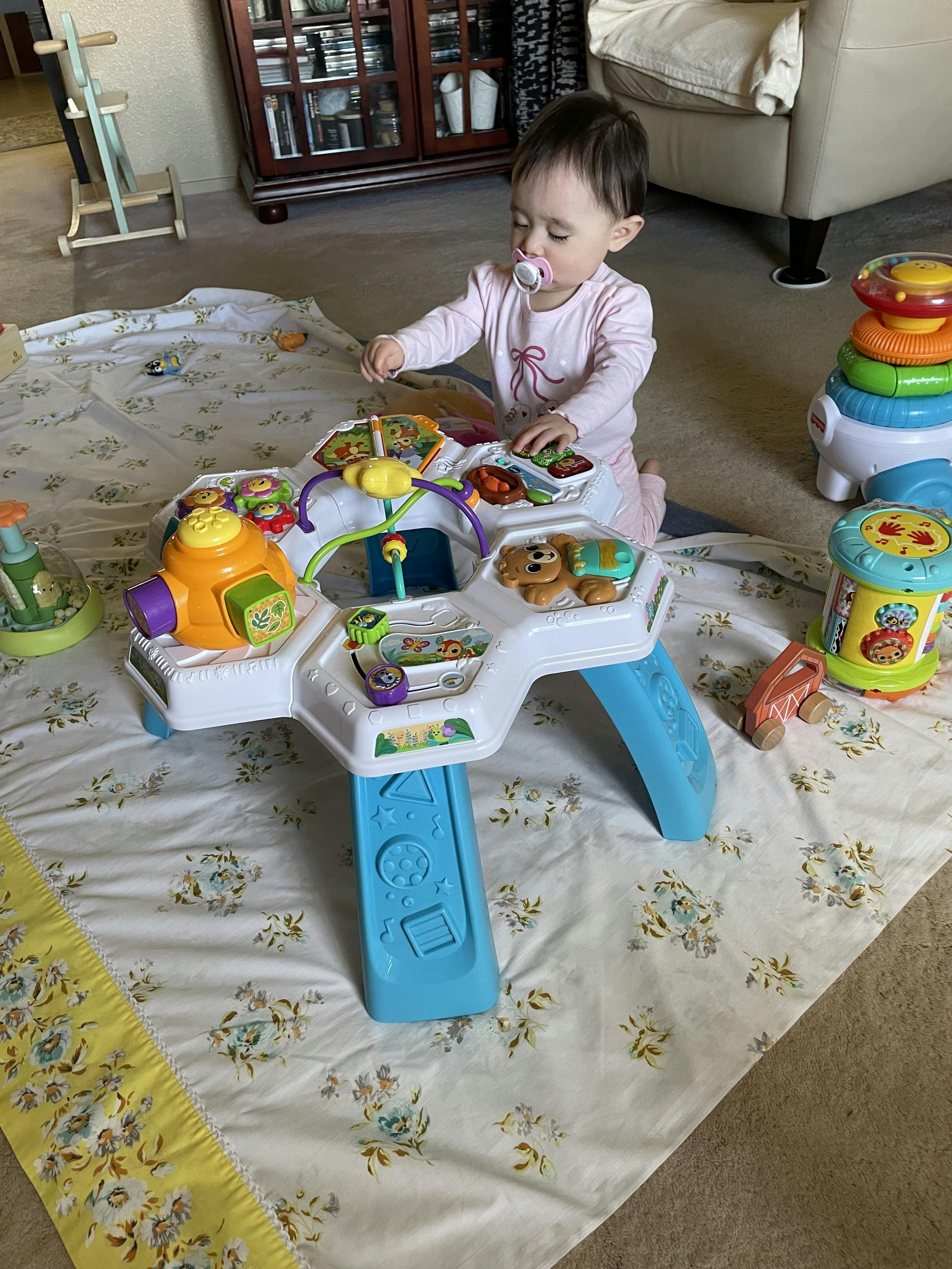 Child kneeling on a patterned blanket, playing with an activity table toy