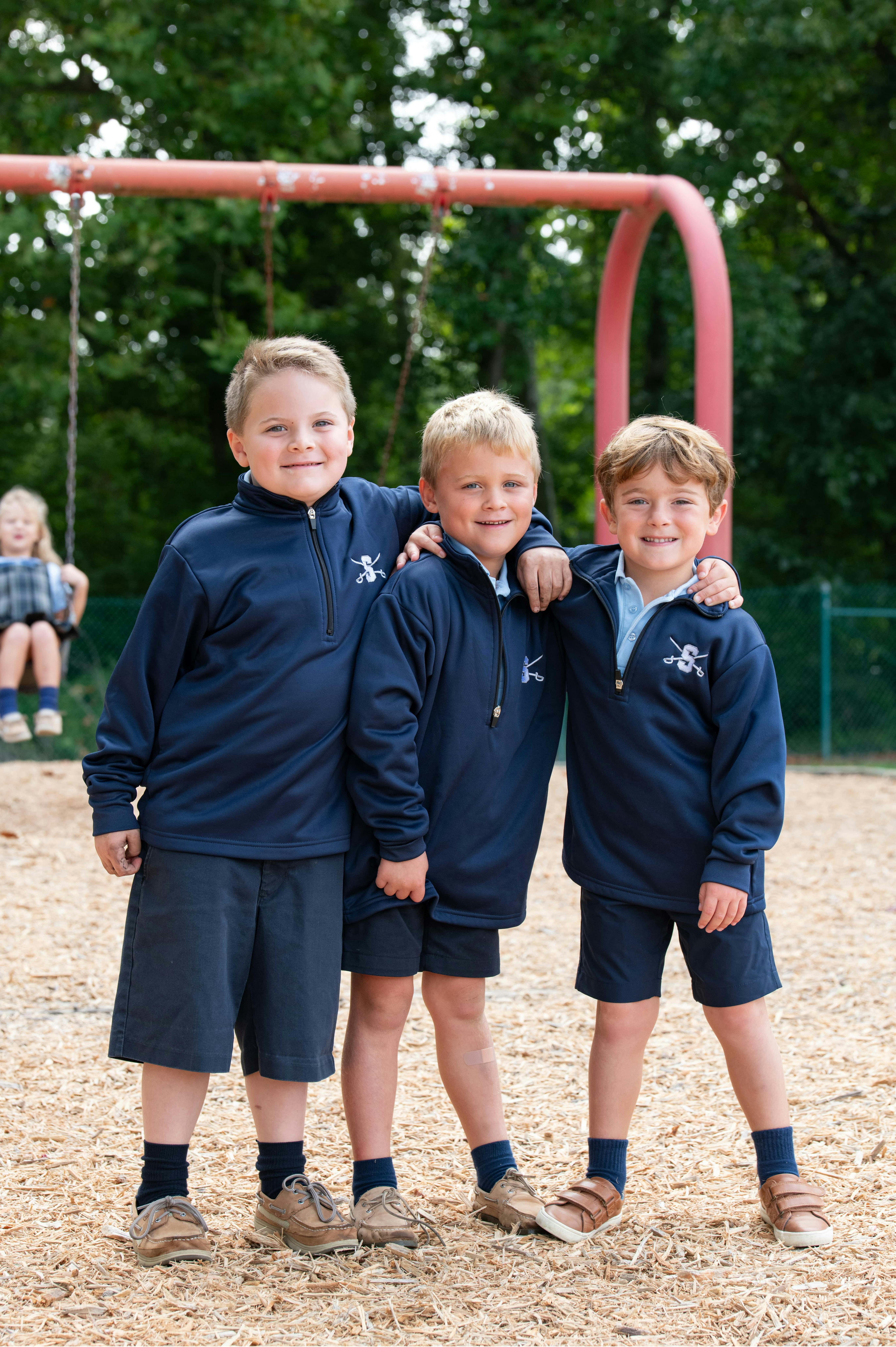 Three children in matching outfits standing together on a playground