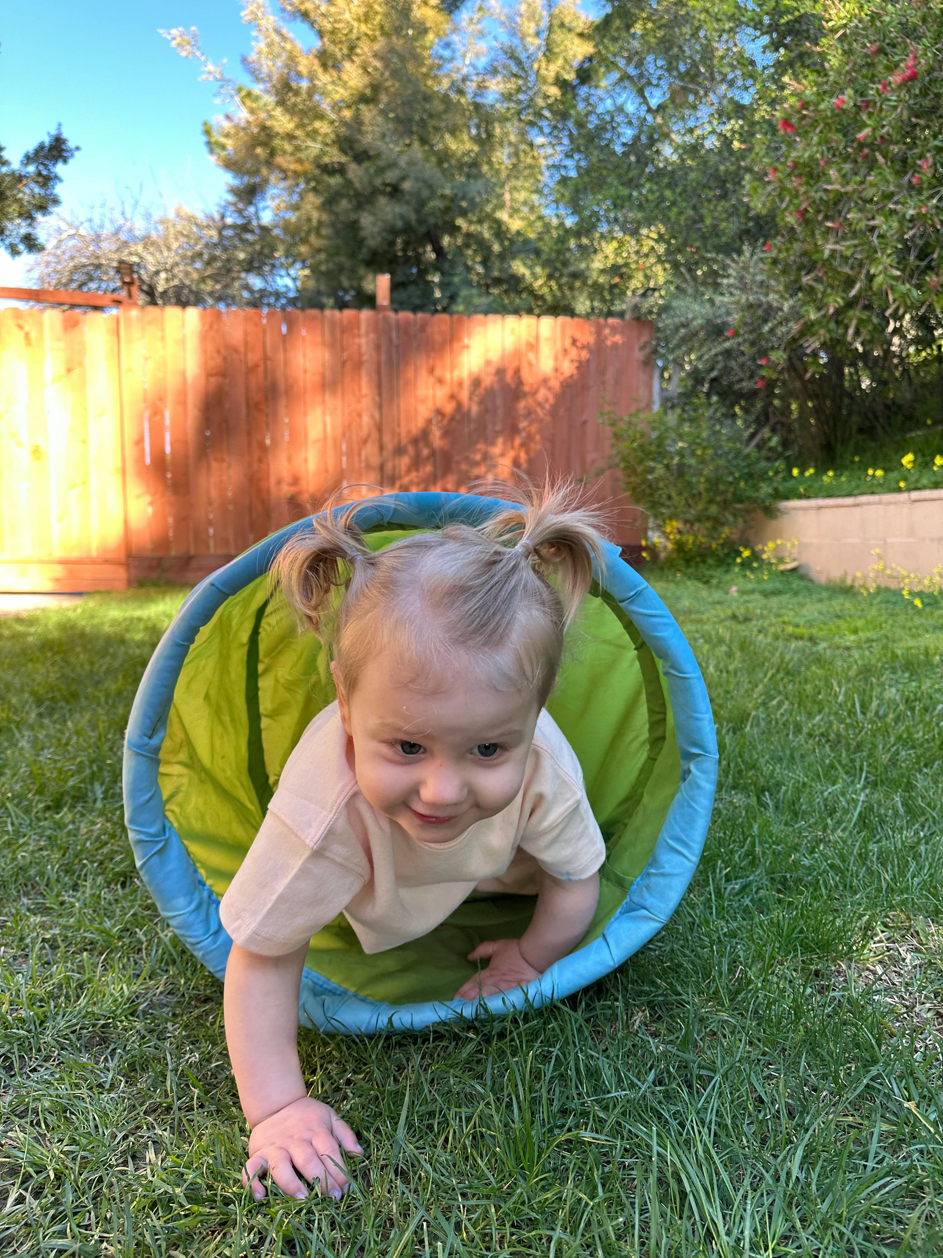 Child crawling out of a play tunnel onto grass