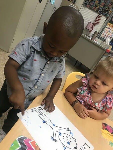Child pointing at a drawing of a person, another child watching
