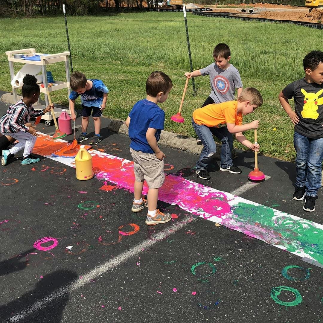Children painting with plungers on a long white paper strip outdoors