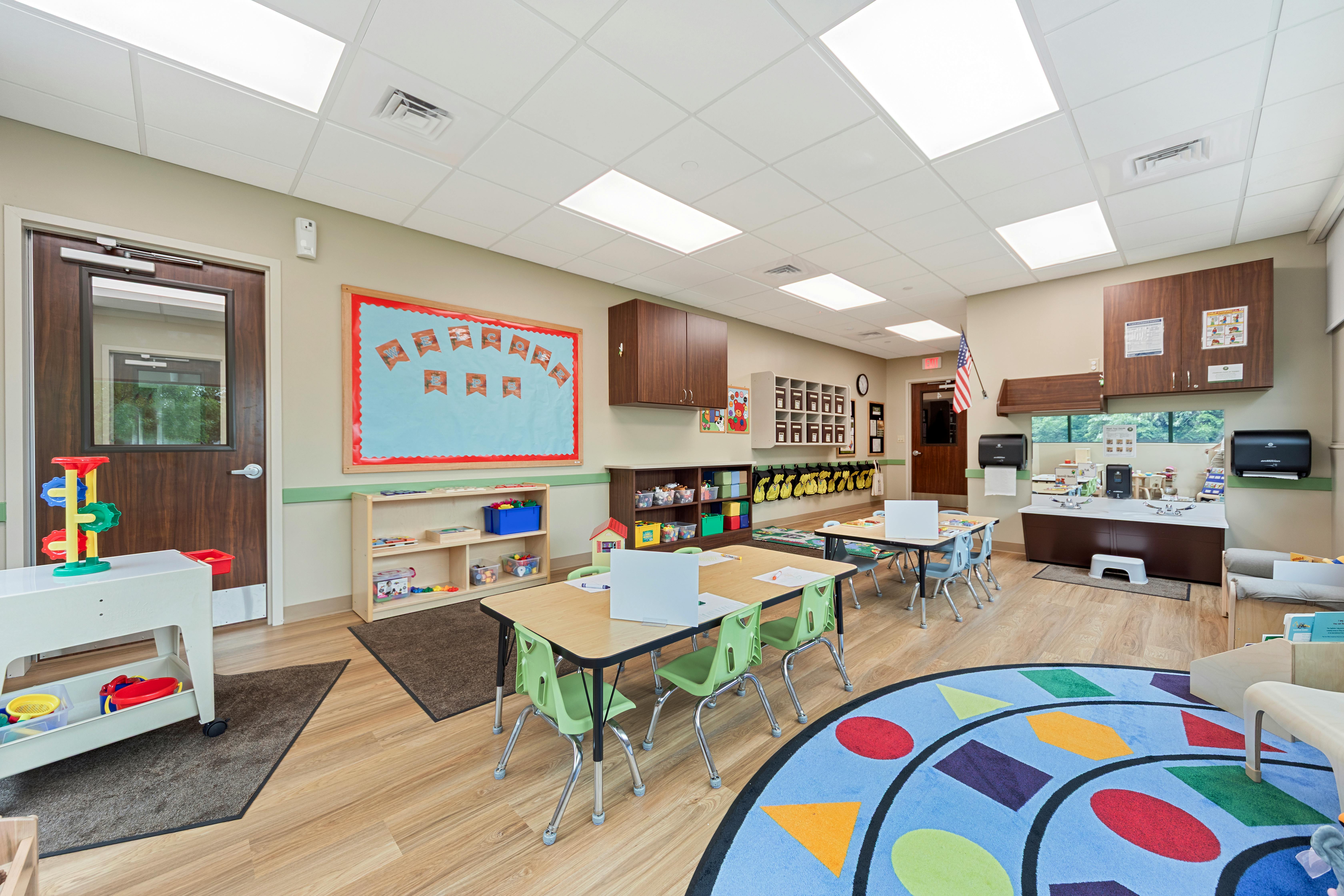 A colorful classroom with small tables and chairs, shelving, and a sink area