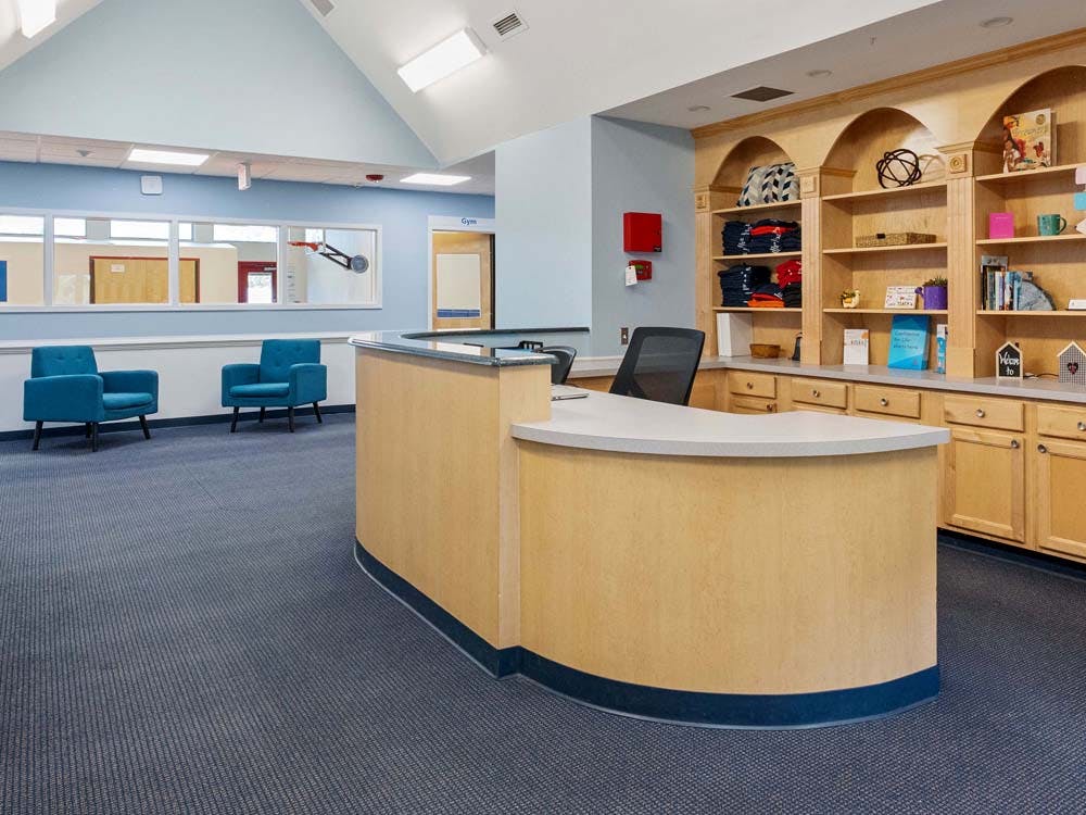 Reception desk with built-in shelves and two blue chairs in a waiting area