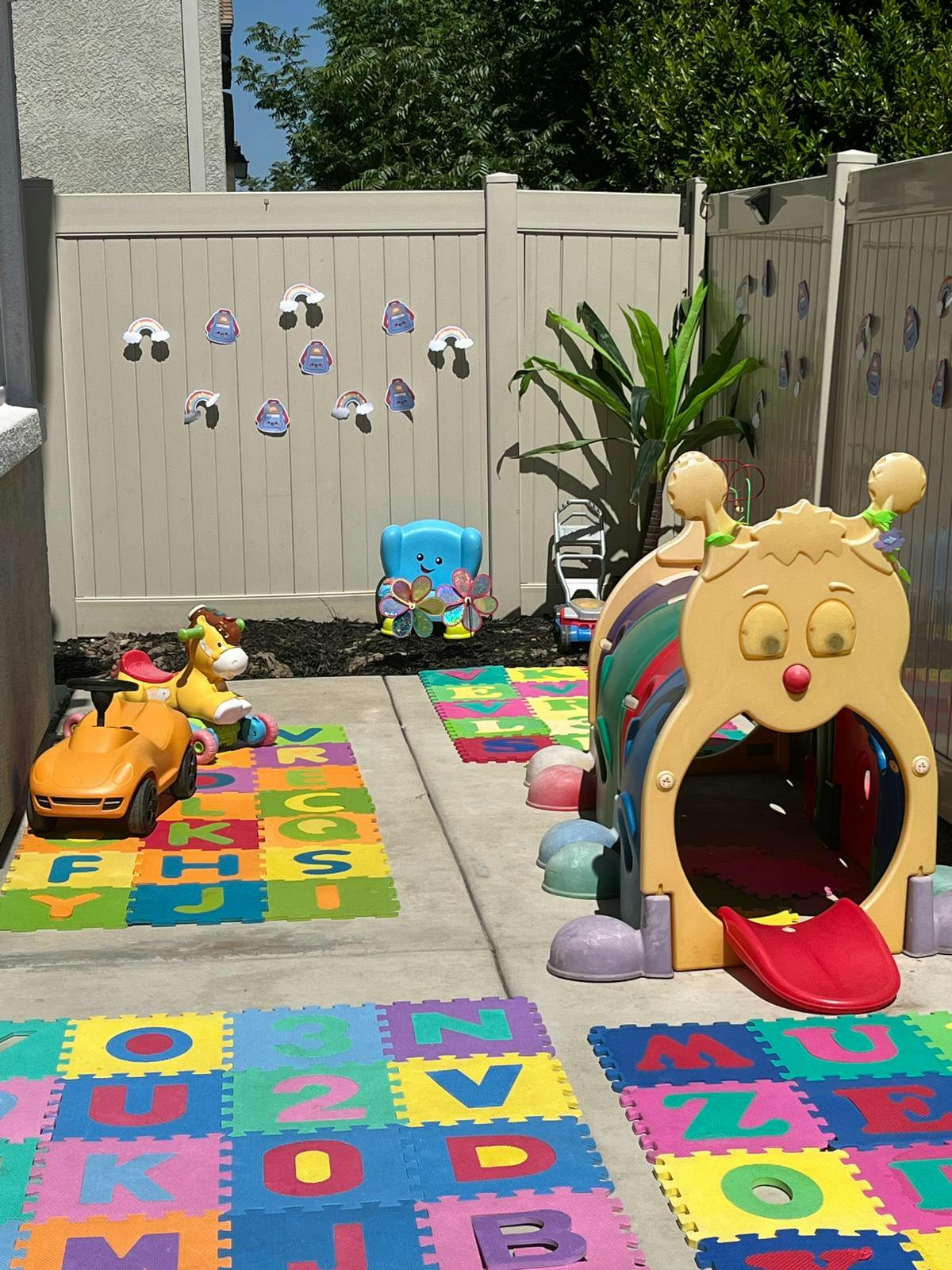 Outdoor play area with colorful alphabet mats and a caterpillar play tunnel