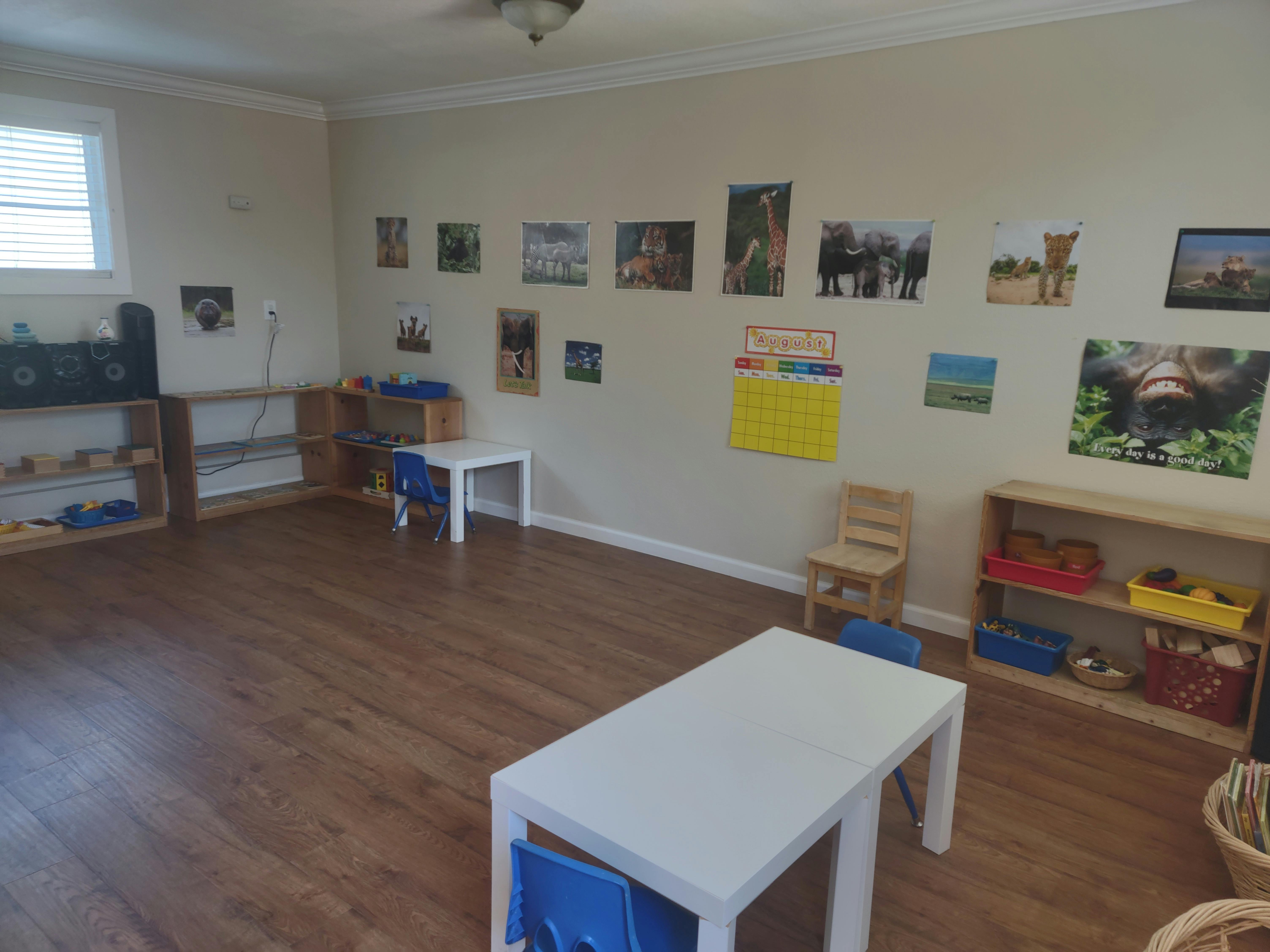 Empty classroom with small tables and chairs, shelves, and pictures on the wall