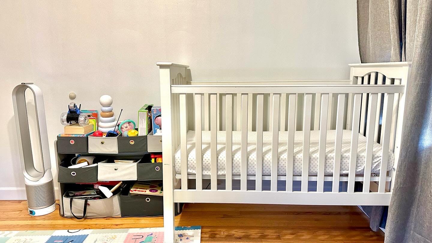 White crib next to a storage unit with toys