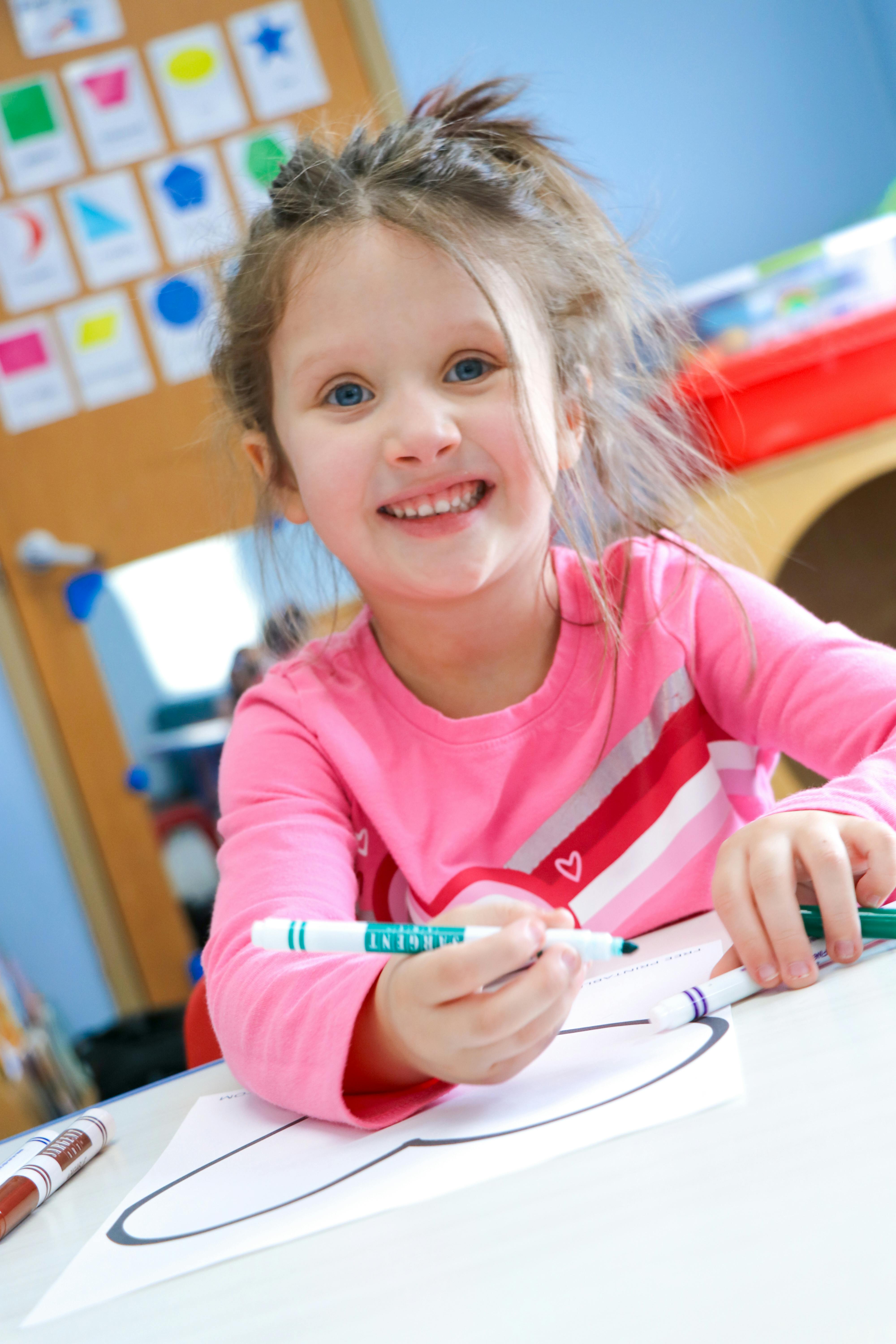 Child drawing on paper with a marker in a classroom