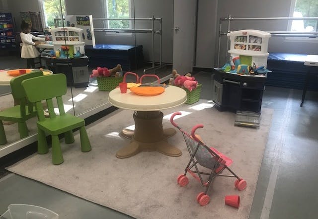 Child in a room with small tables, chairs, and a toy stroller