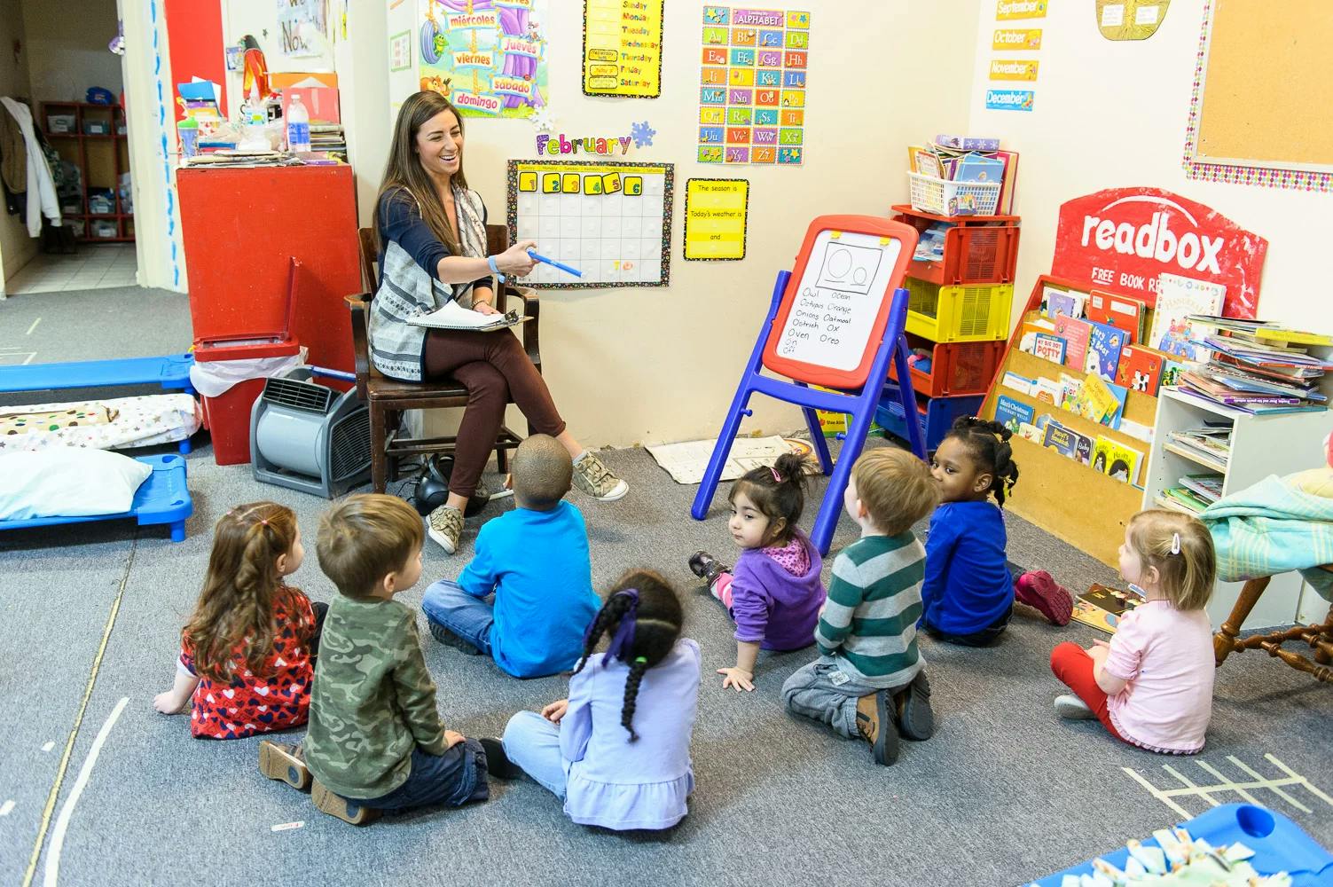 Person sitting on a chair reading to a group of children in a classroom