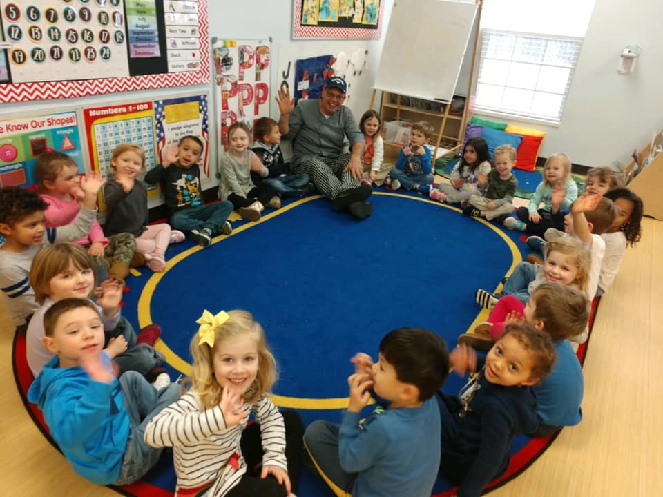 Adult and children sitting in a circle on a blue rug in a classroom