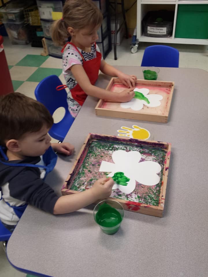 Two children painting shamrock cutouts at a table