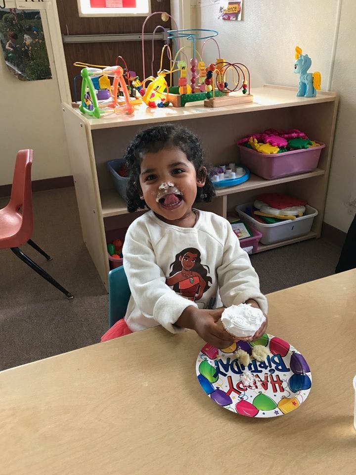 Child with frosting on face and tongue out, holding a cupcake