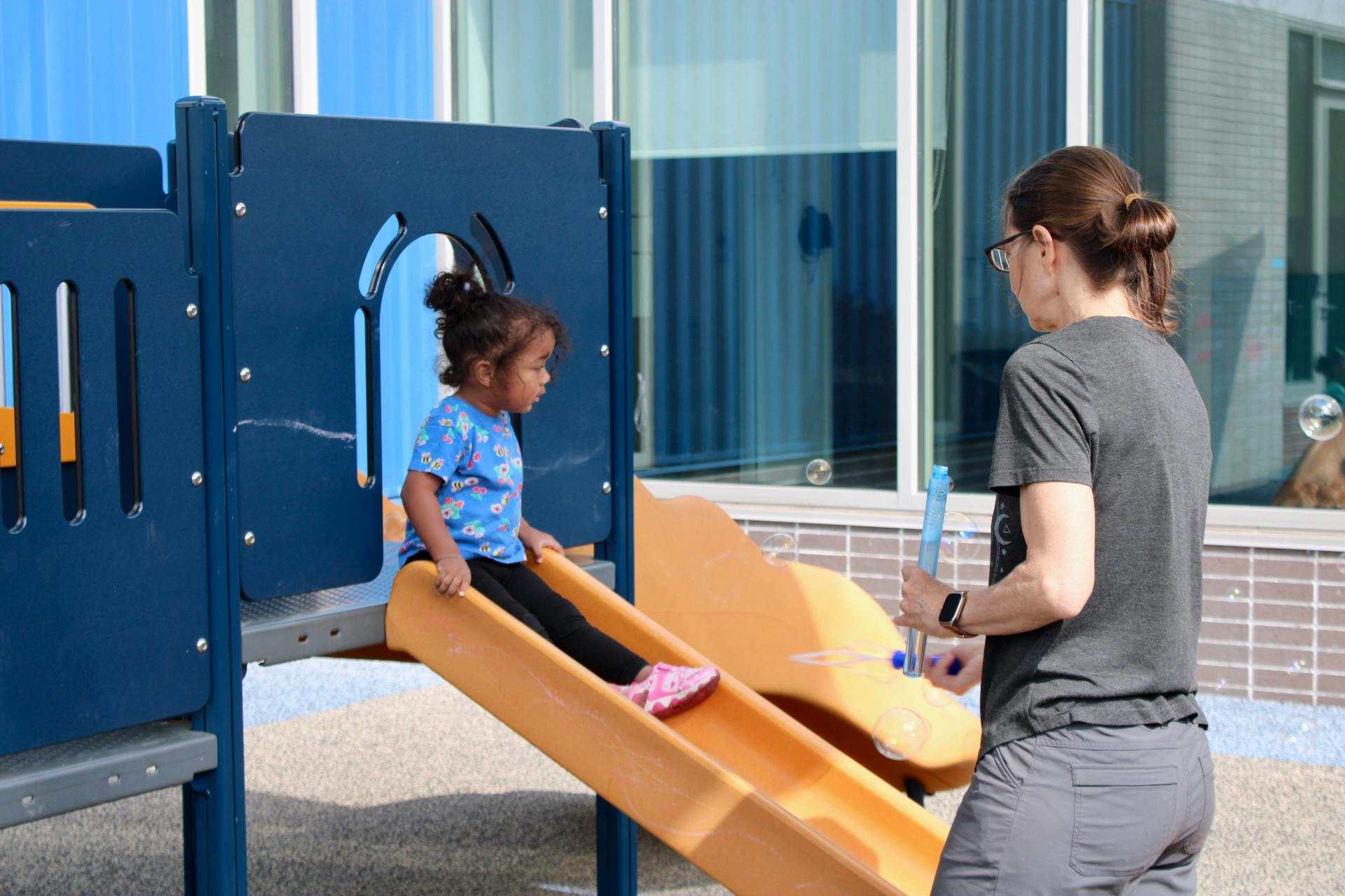 Child on a slide with a person standing nearby