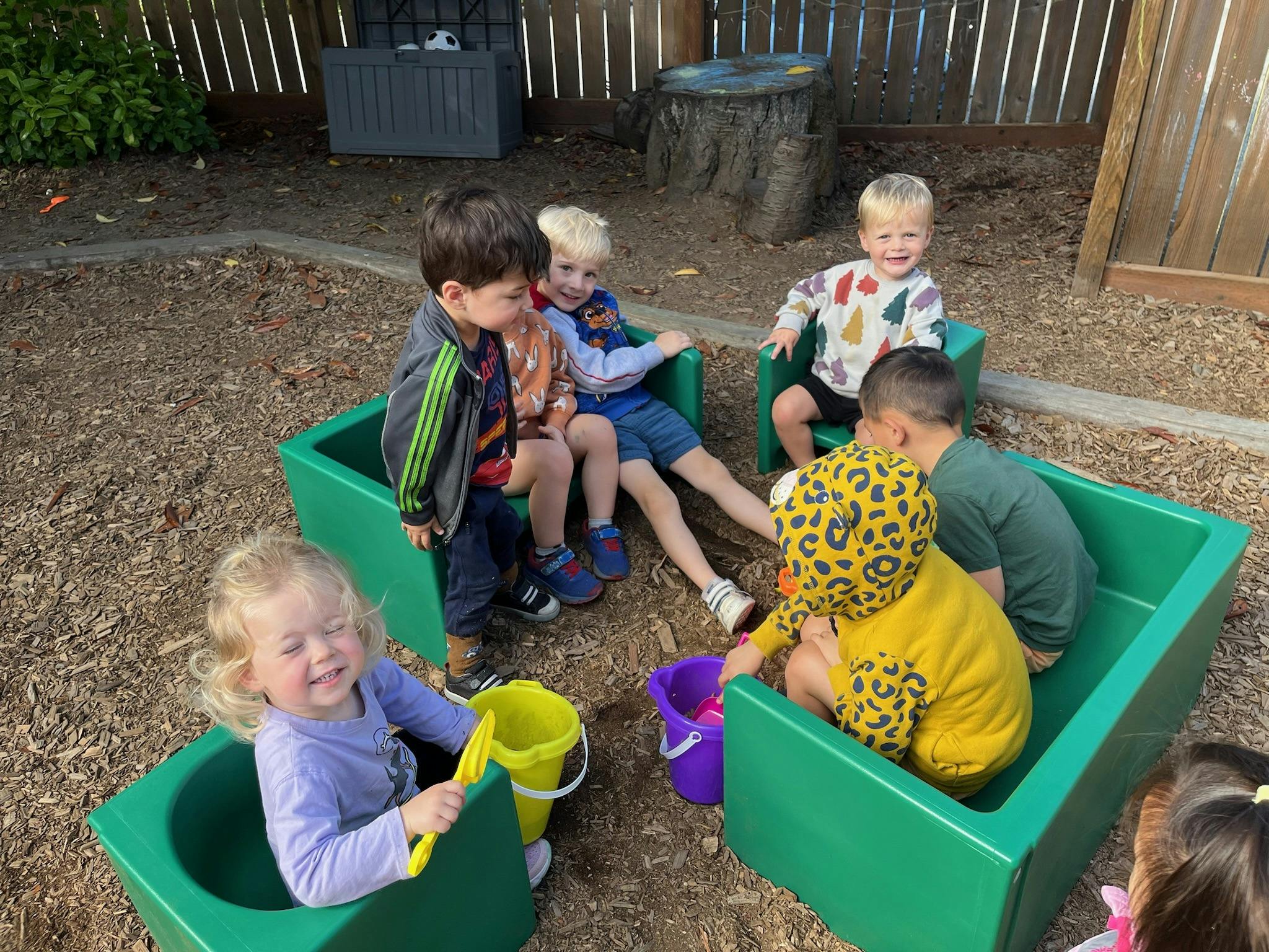 Group of children playing outdoors in green containers with buckets