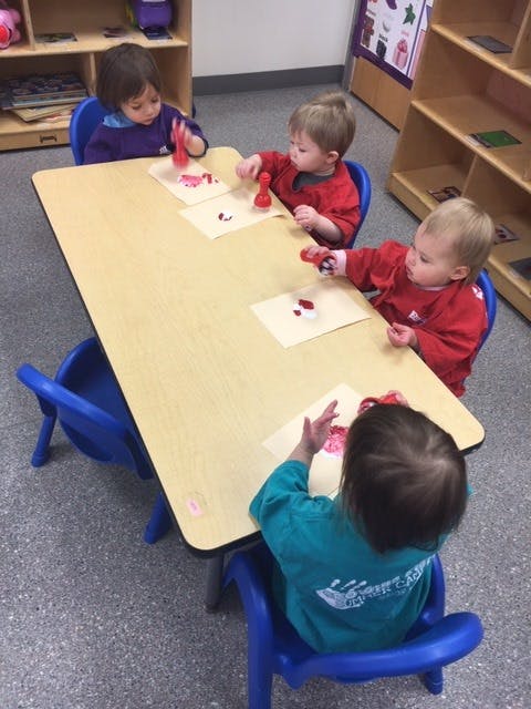 Four children at a table doing an art activity with red paint