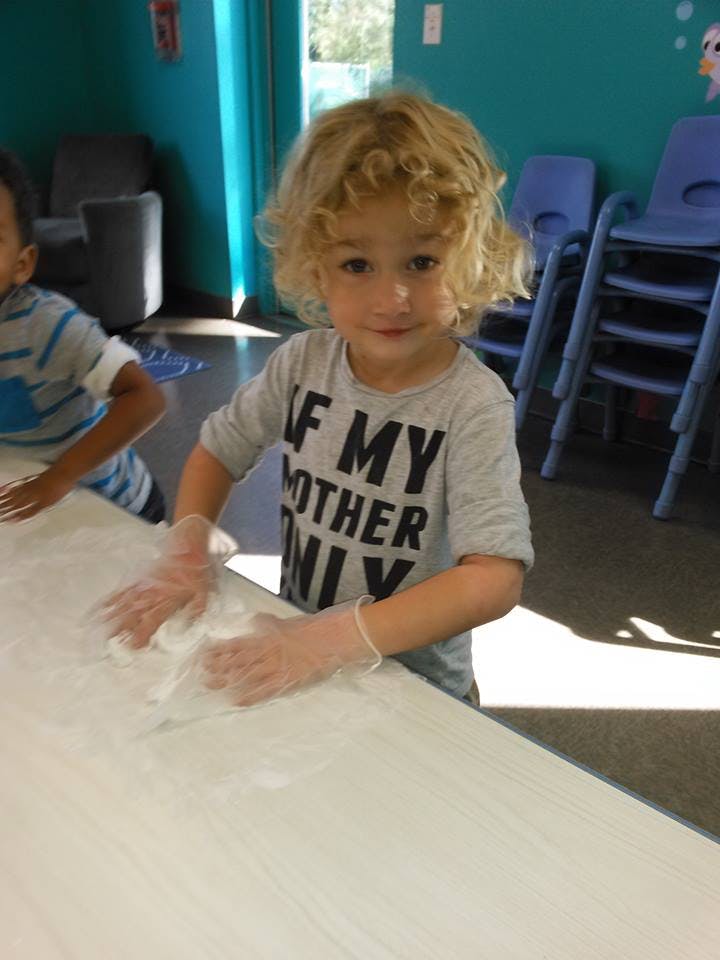 Child wearing gloves and playing with white material on a table