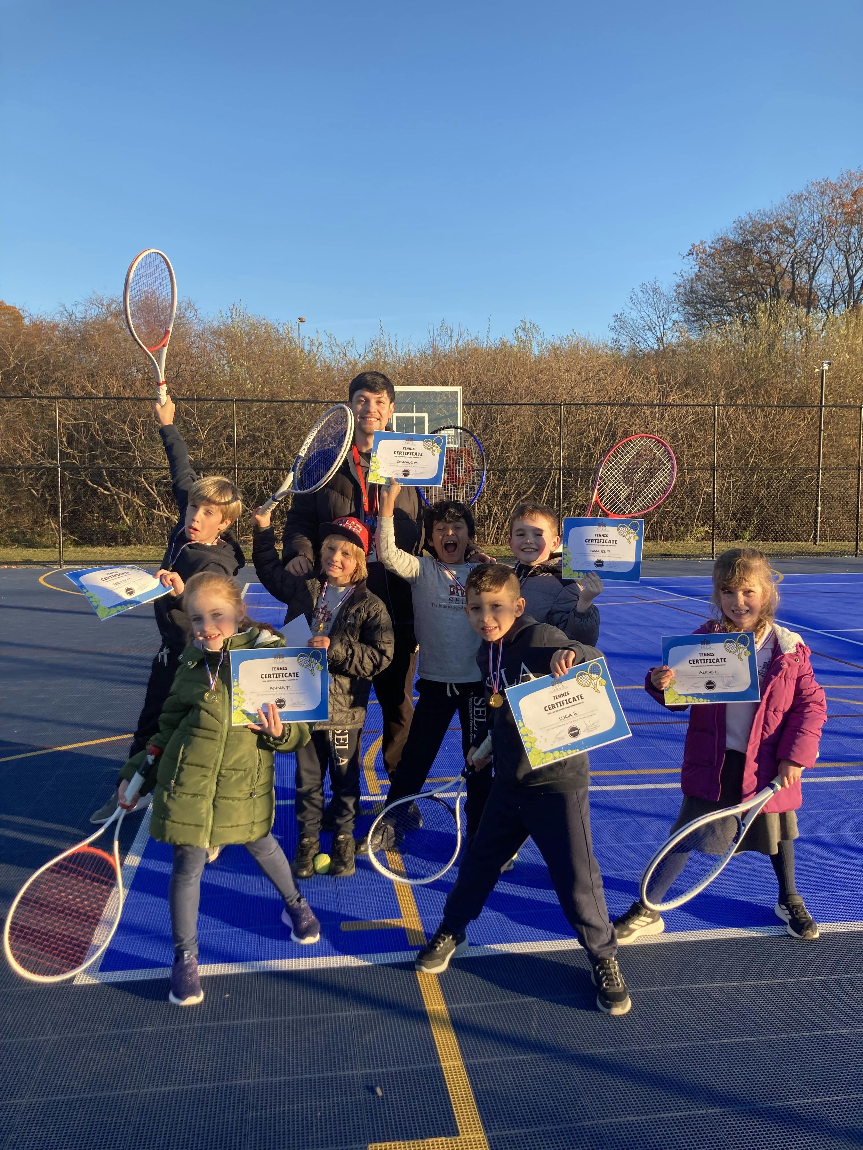 Group of children and a person holding tennis rackets and certificates on a court