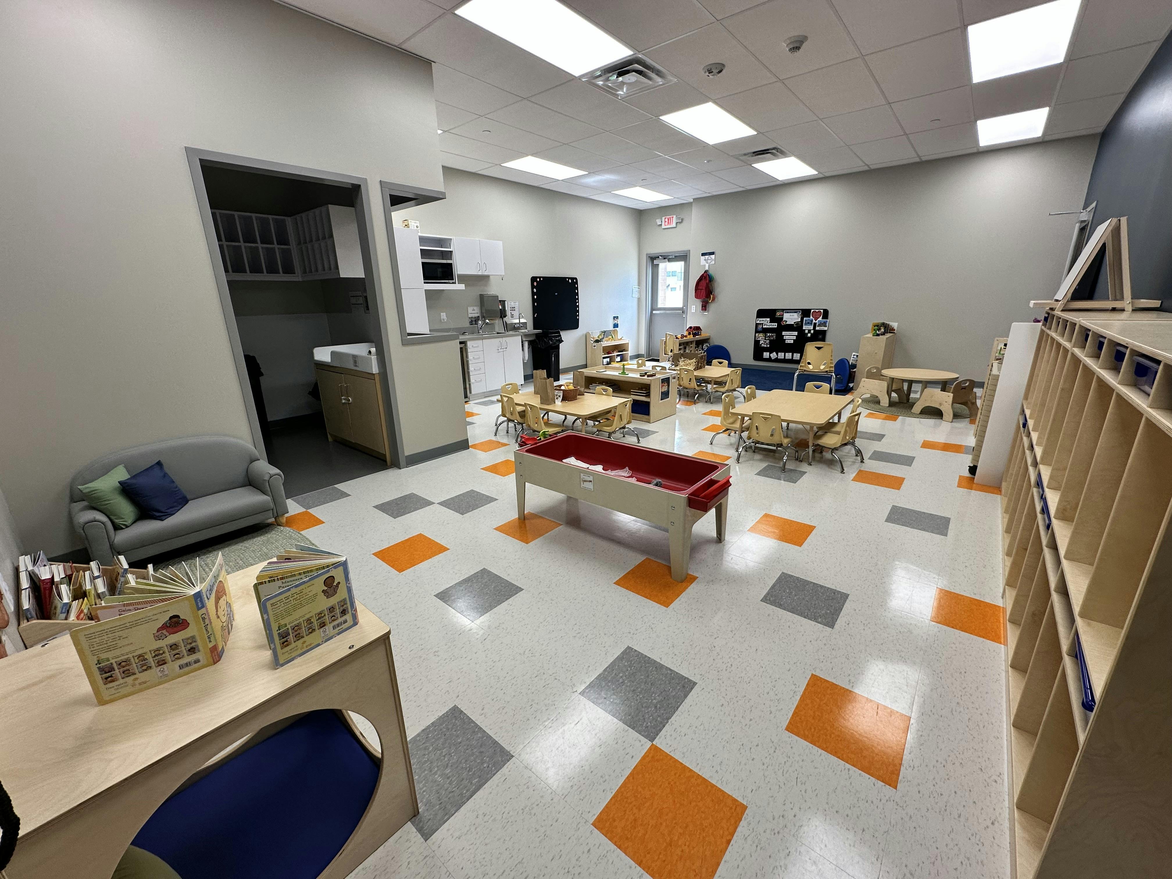 Empty classroom with small tables and chairs, a couch, and a play bin