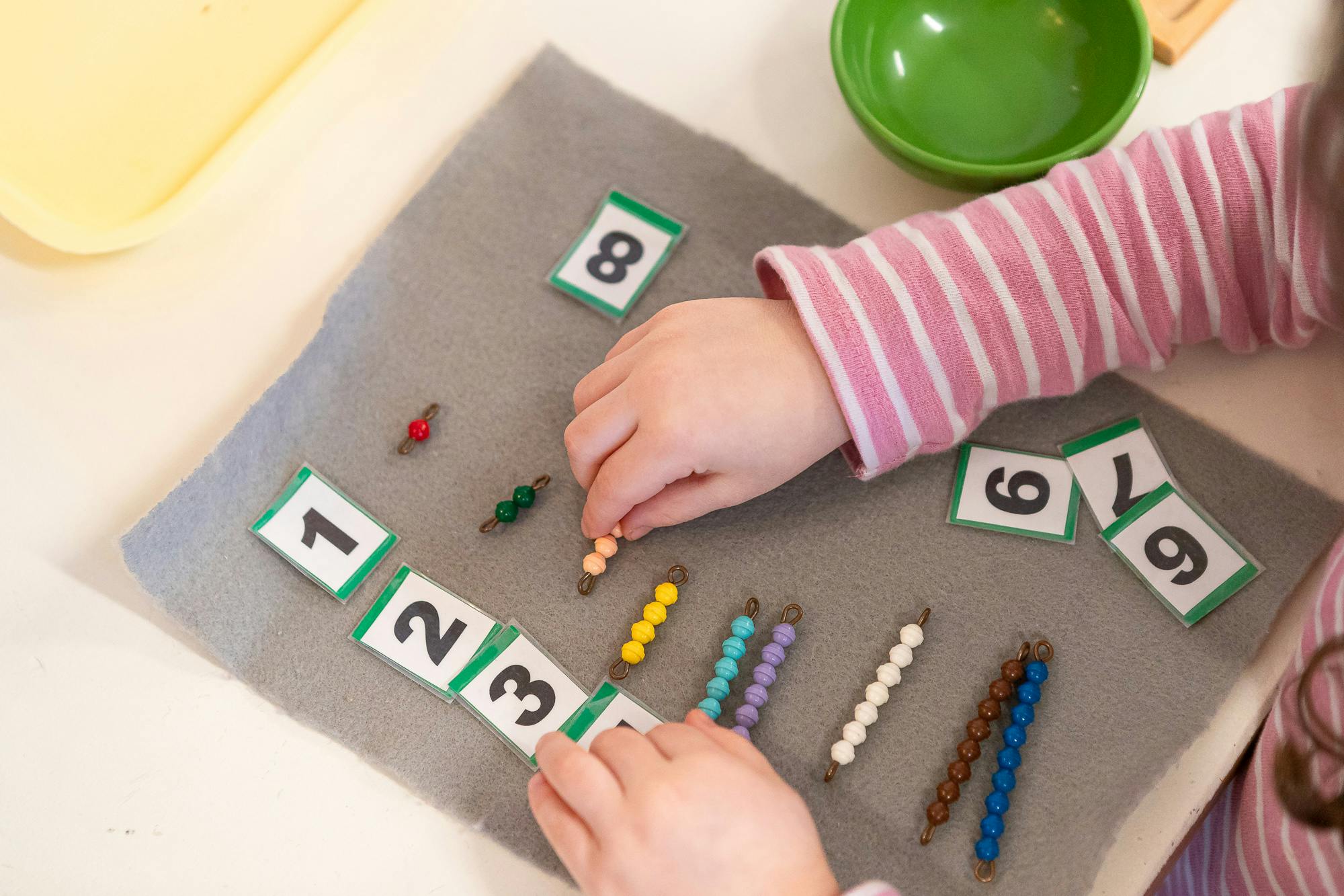Child's hands arranging number cards and counting beads on a mat