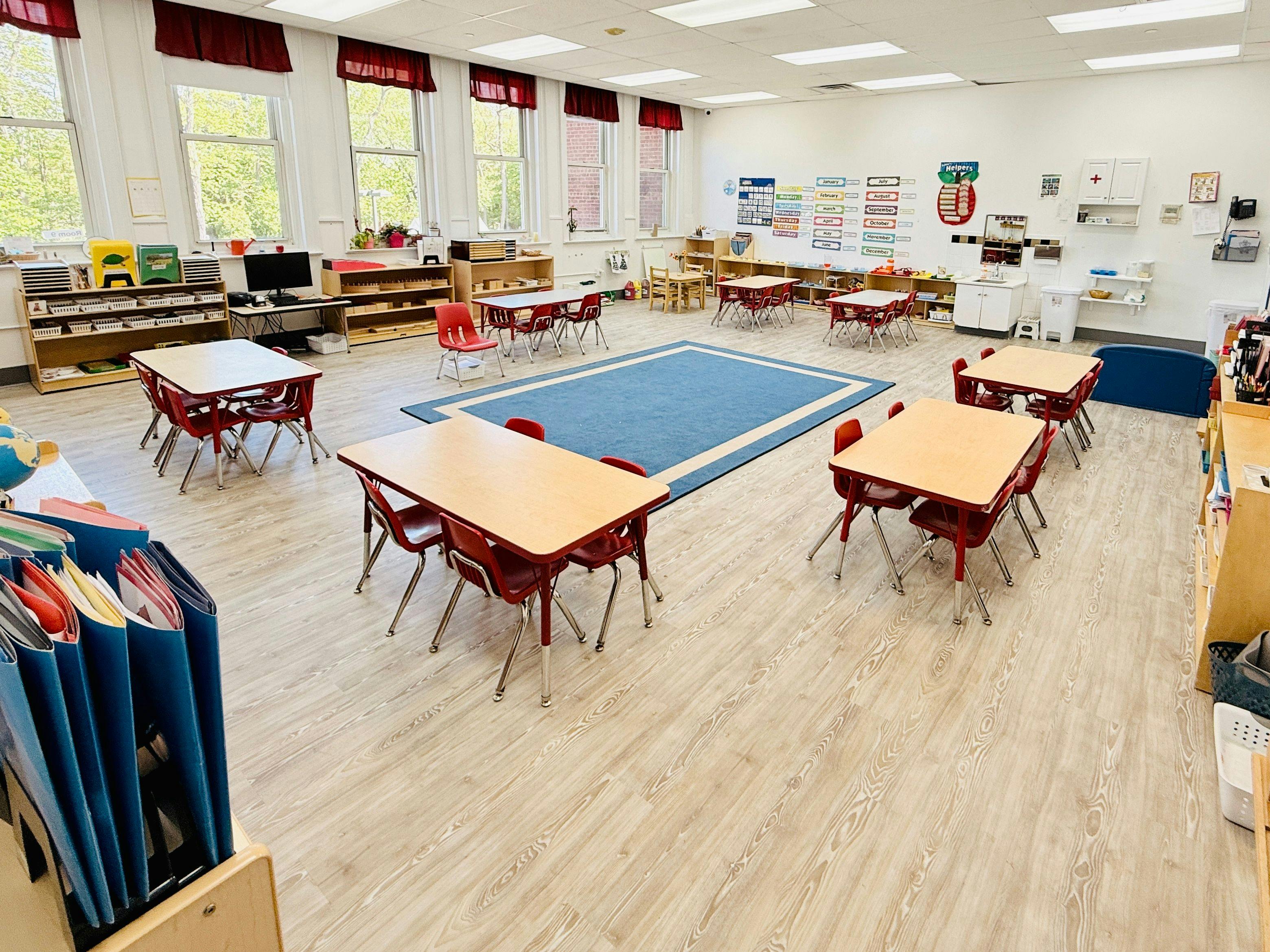 Classroom with small tables and chairs, and a blue rug on the floor