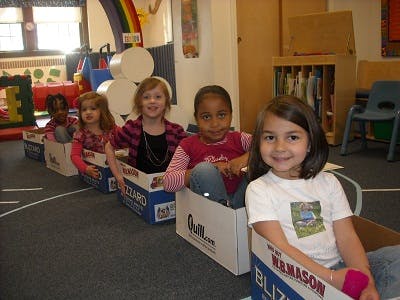 Four children sitting in cardboard boxes in a line