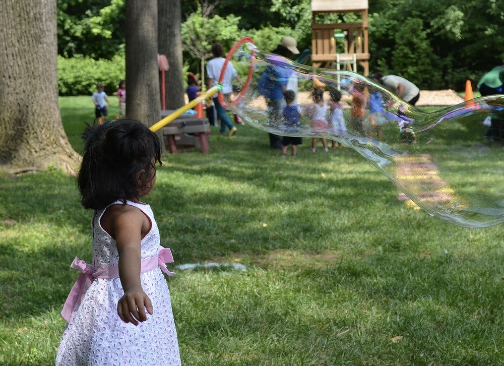 Child watching people making large bubbles in a grassy area