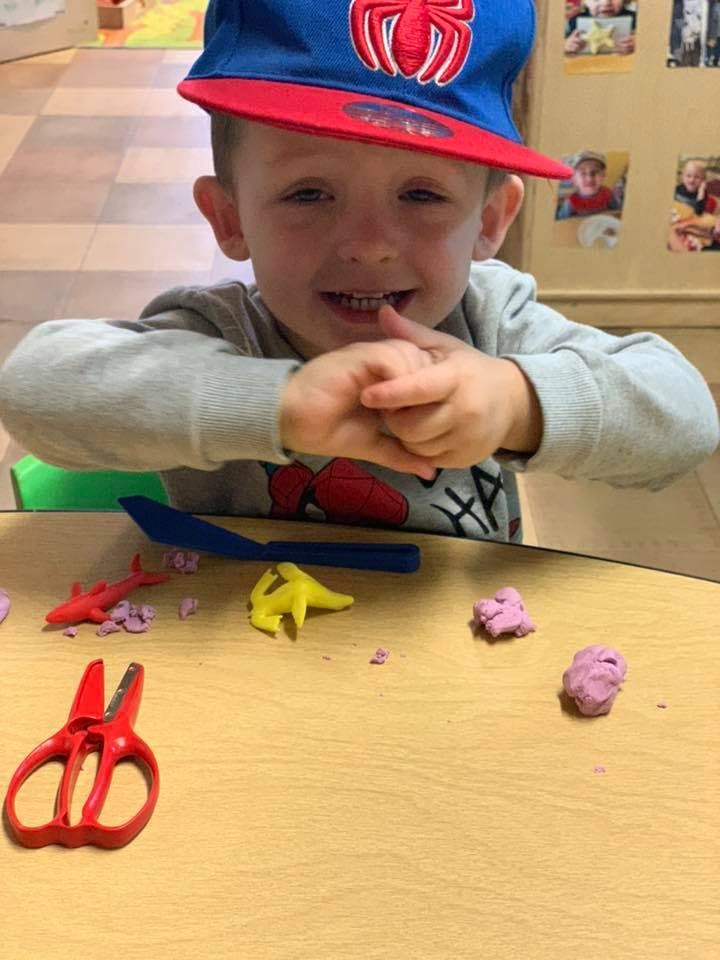 Child in a baseball cap playing with modeling clay and scissors at a table