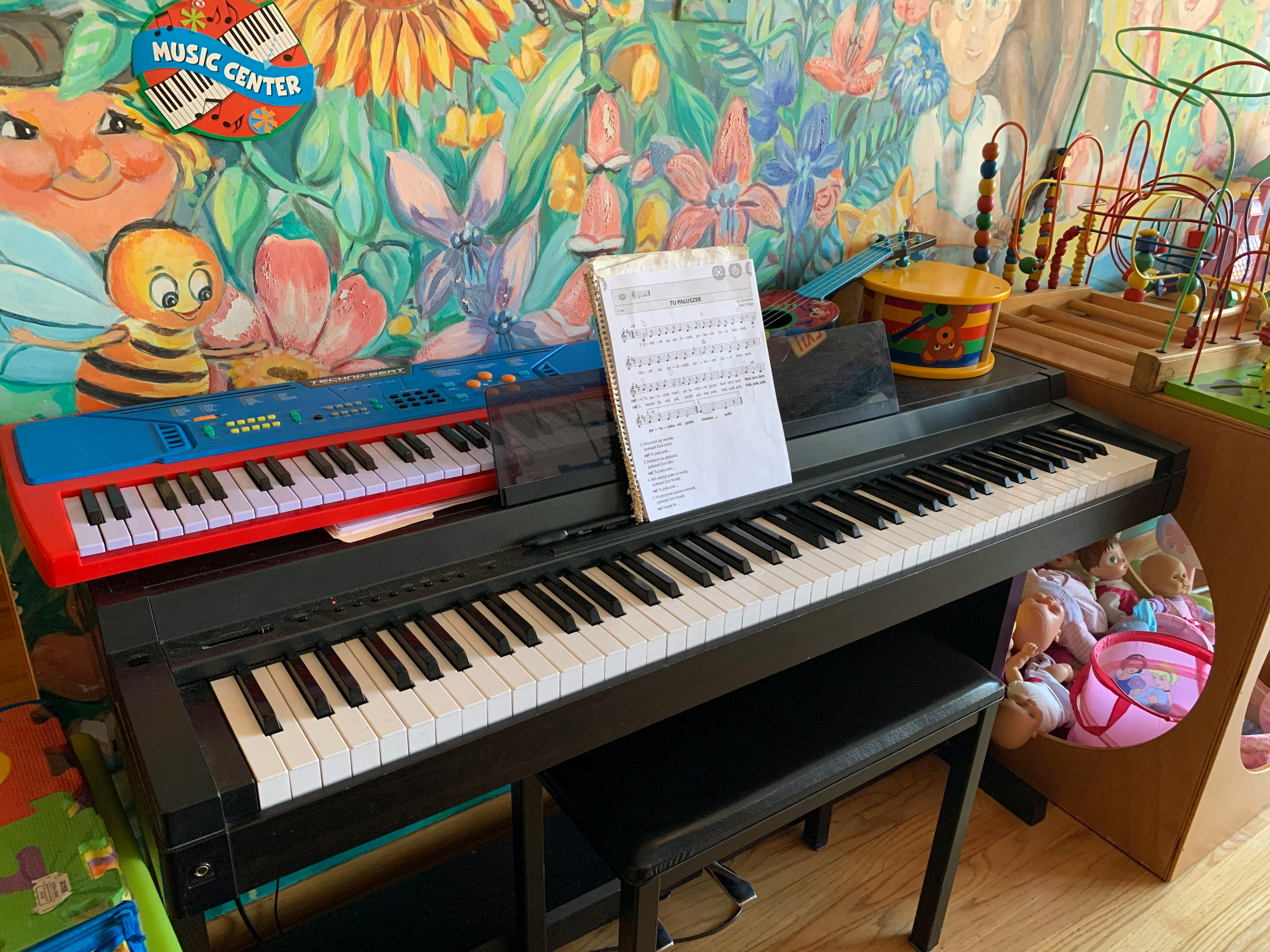 Two keyboards with sheet music on a stand in front of a colorful mural