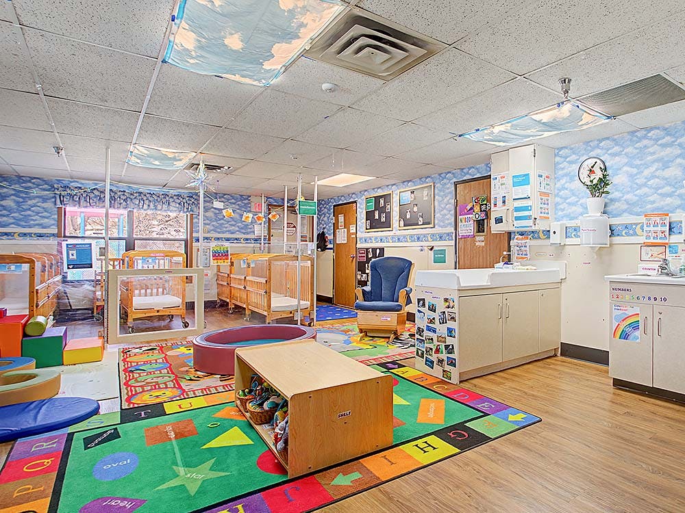 A colorful daycare room with cribs, play mats, and changing stations