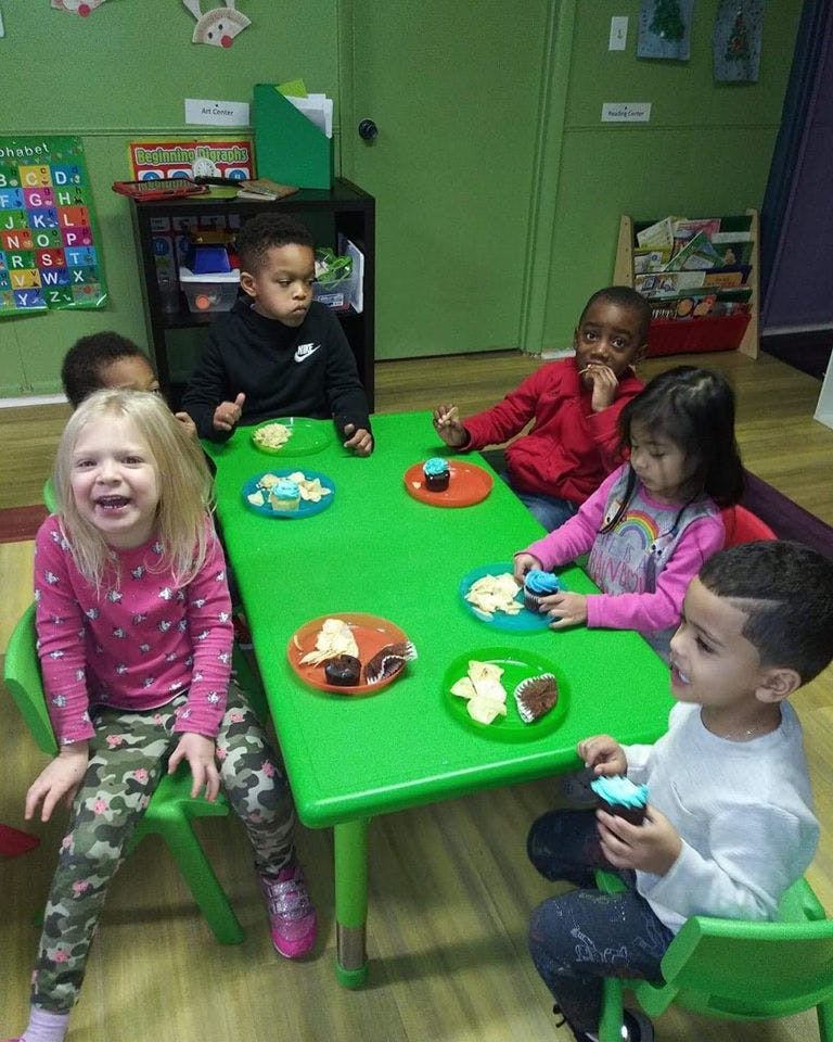 Children sitting at a green table with plates of food