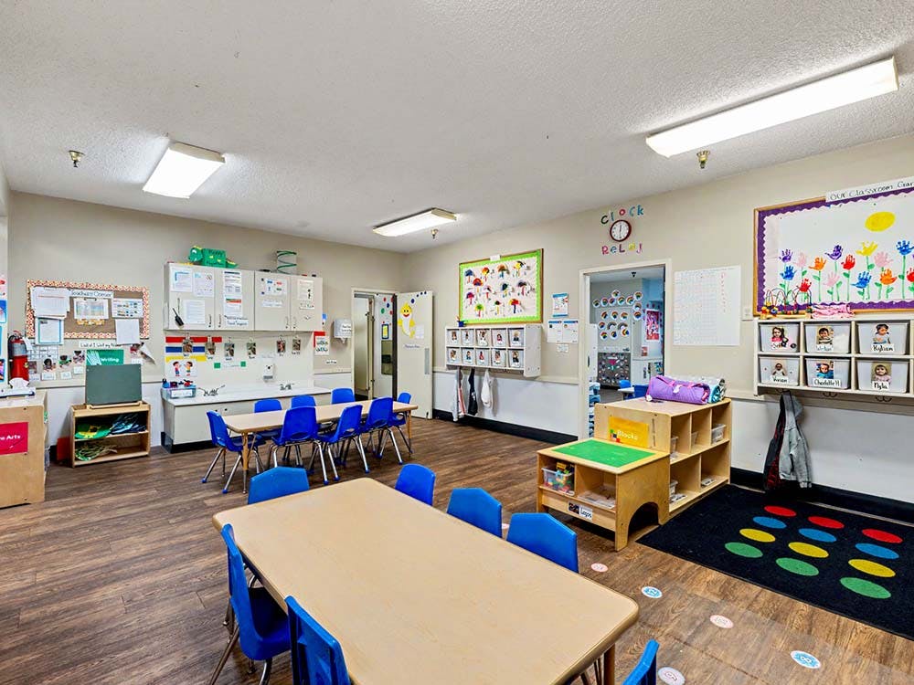 Empty classroom with tables and blue chairs, decorated with children's art