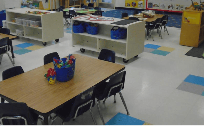 Classroom with tables and chairs, shelves with bins, and colorful floor tiles