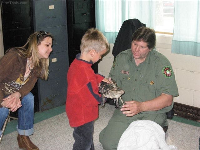 Adult and child looking at a fish held by a person in uniform