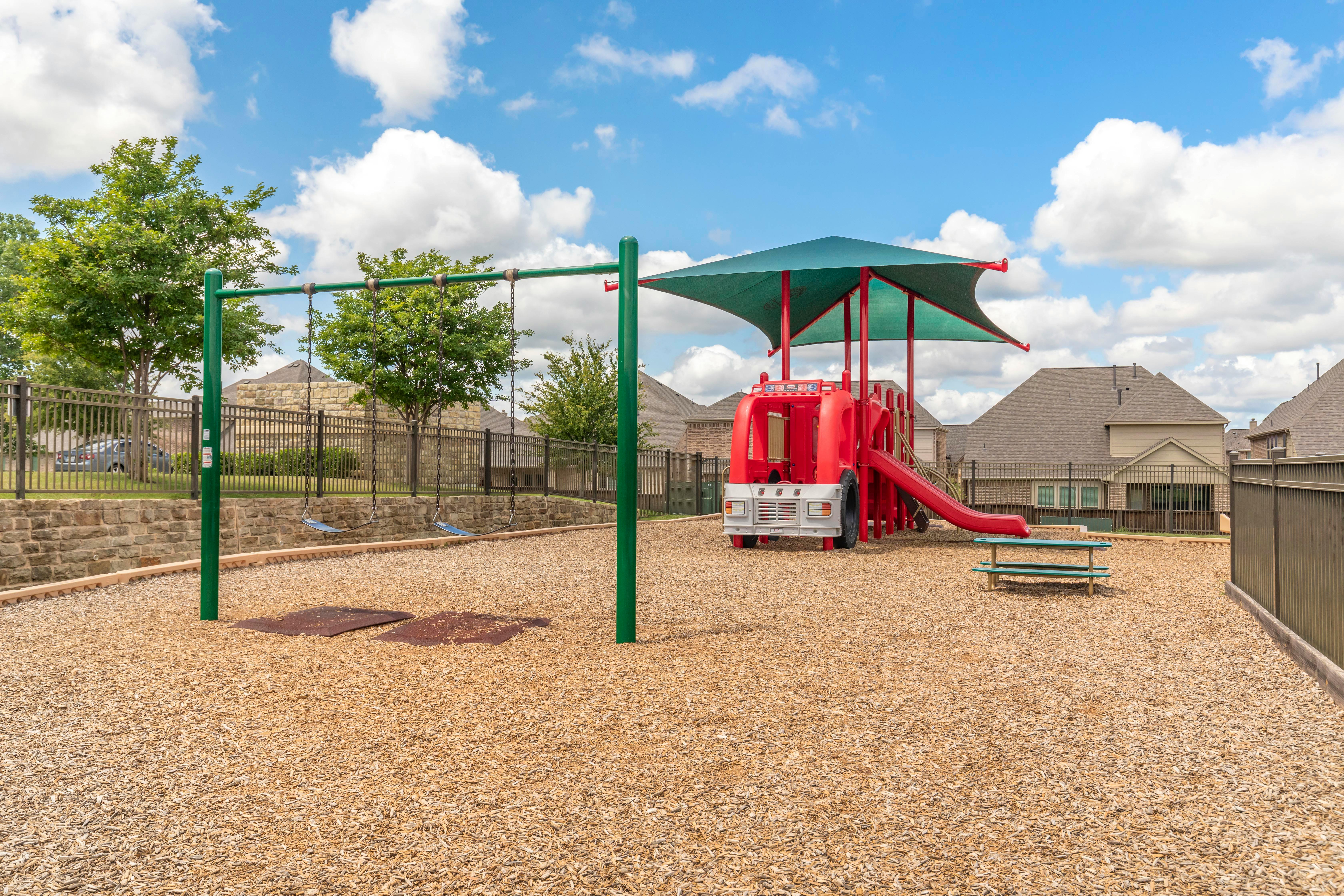 A colorful playground with a red fire truck structure, slide, and green swings
