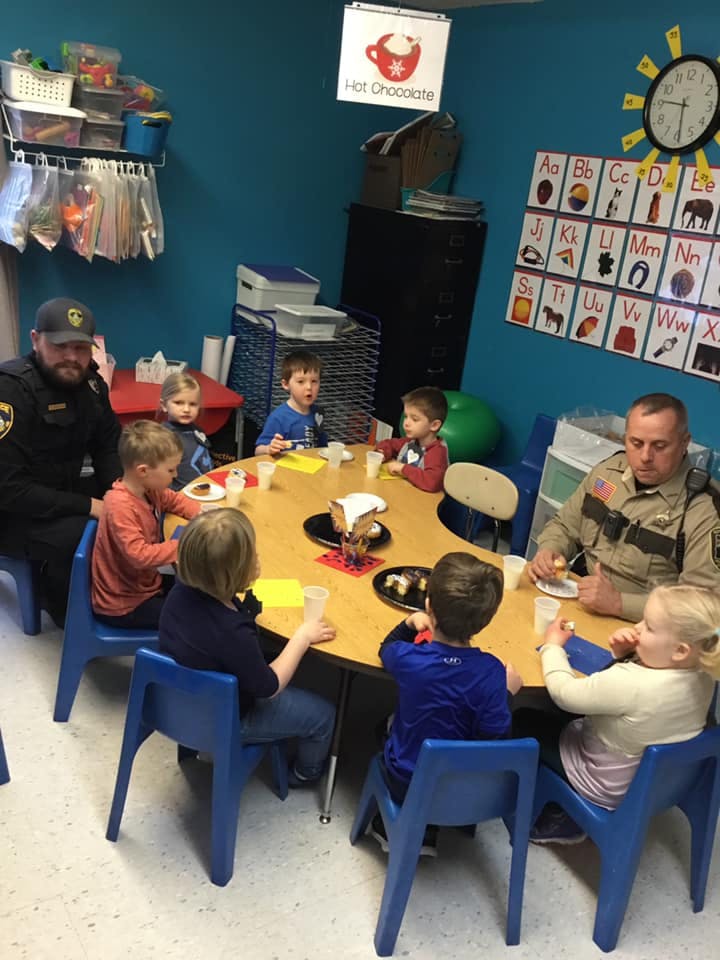 Two people in uniform and several children sitting around a table