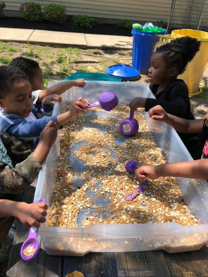 Children playing with scoops in a sensory bin filled with oats