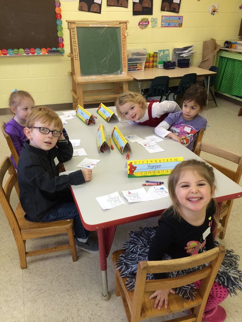Four children and one teen sitting at a table in a classroom