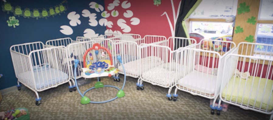 Multiple white cribs and a baby activity center in a room