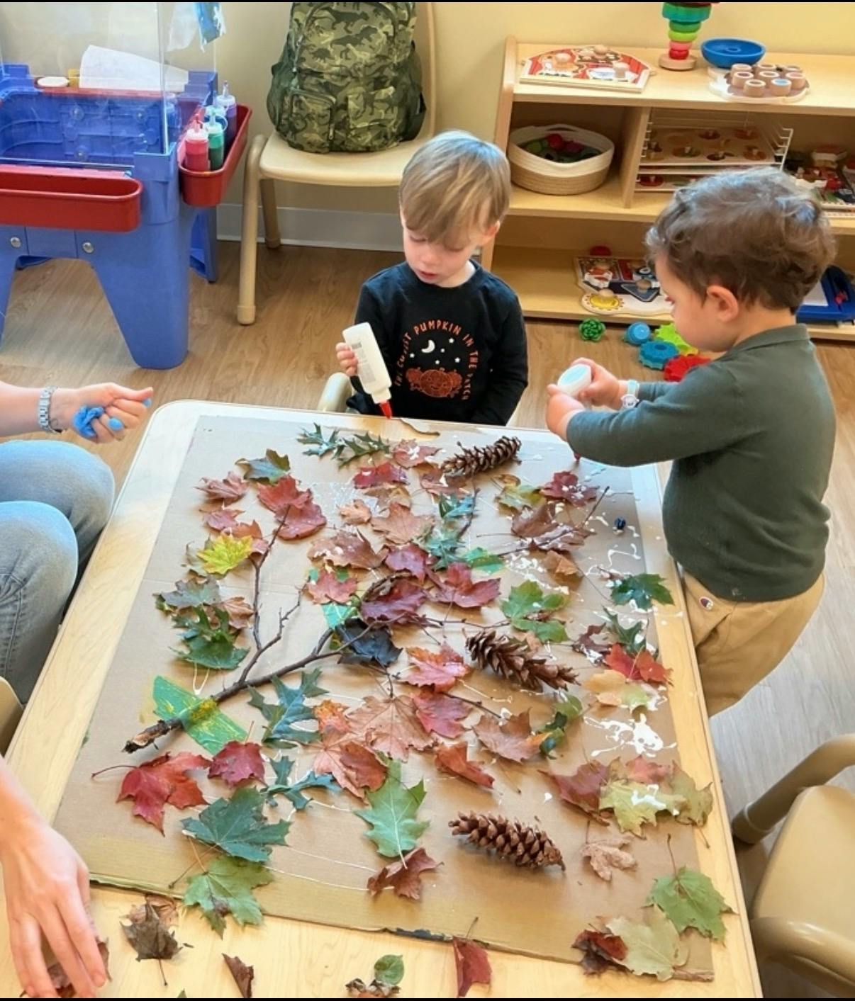 Two children making an art project with autumn leaves and glue on cardboard