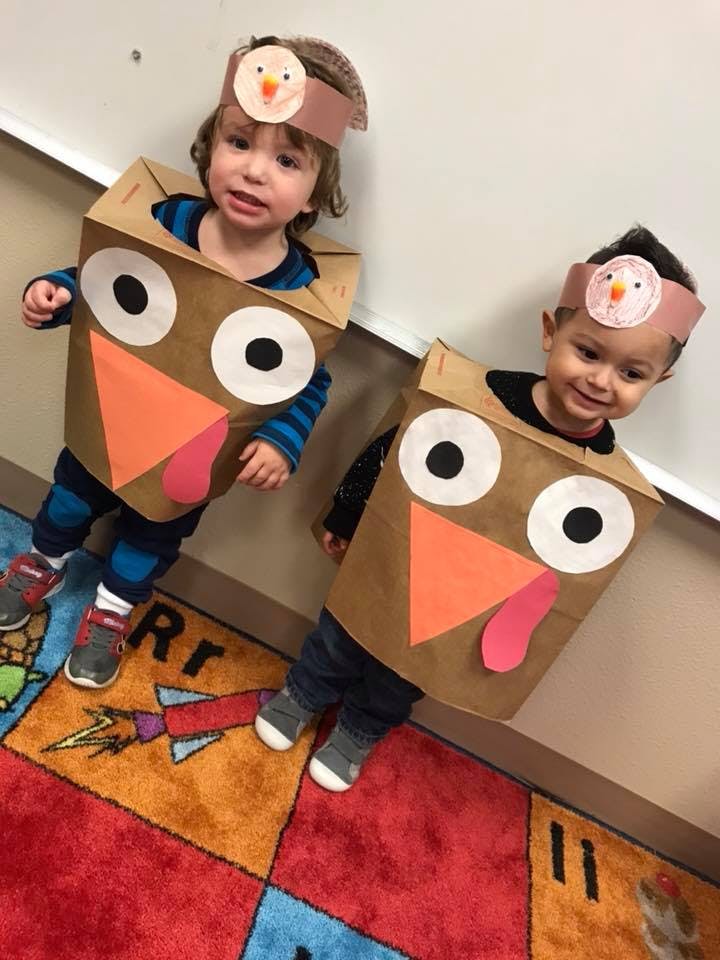 Two children wearing turkey costumes made from paper bags and headbands