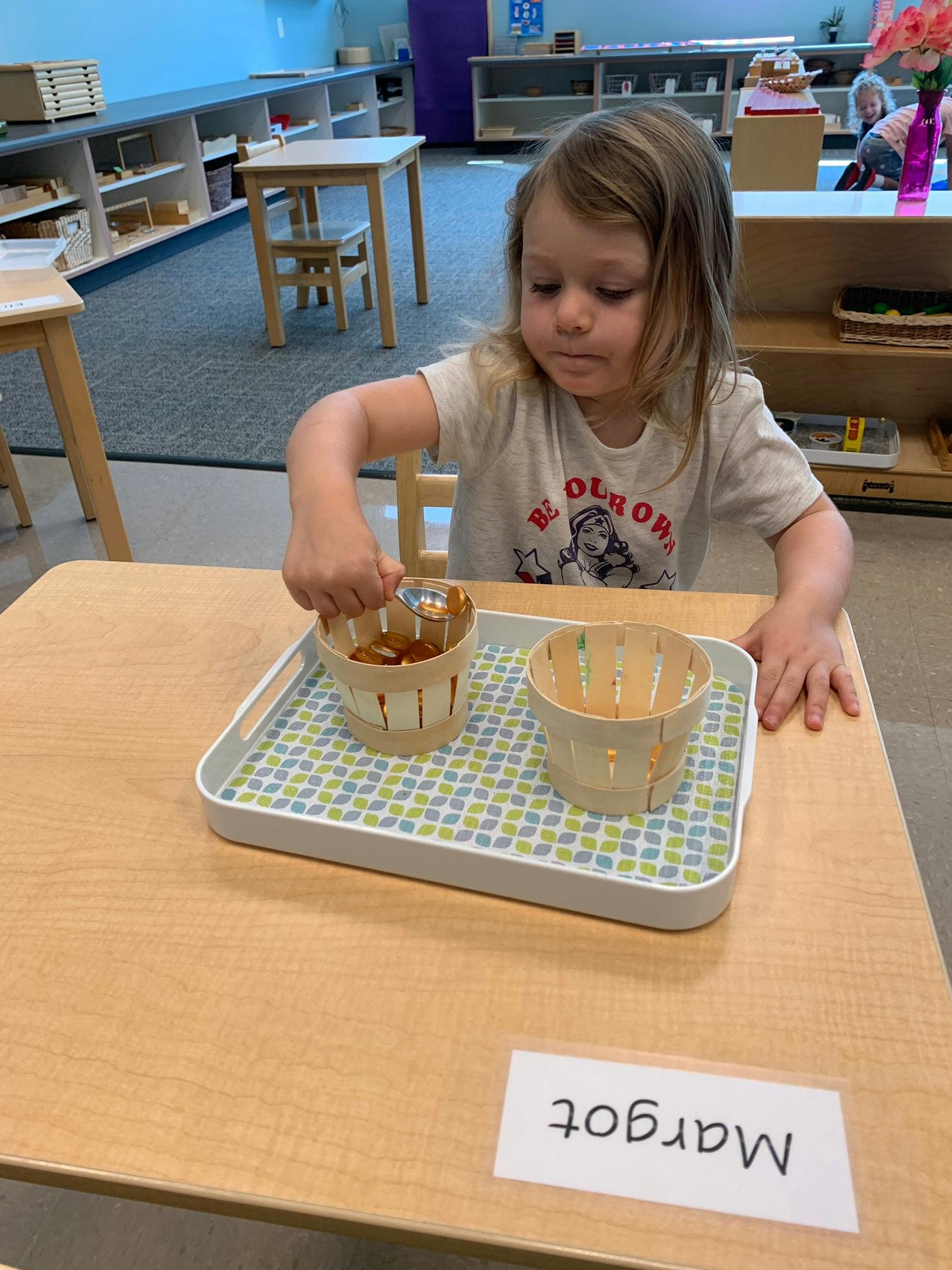 Child scooping small objects from one basket to another on a tray