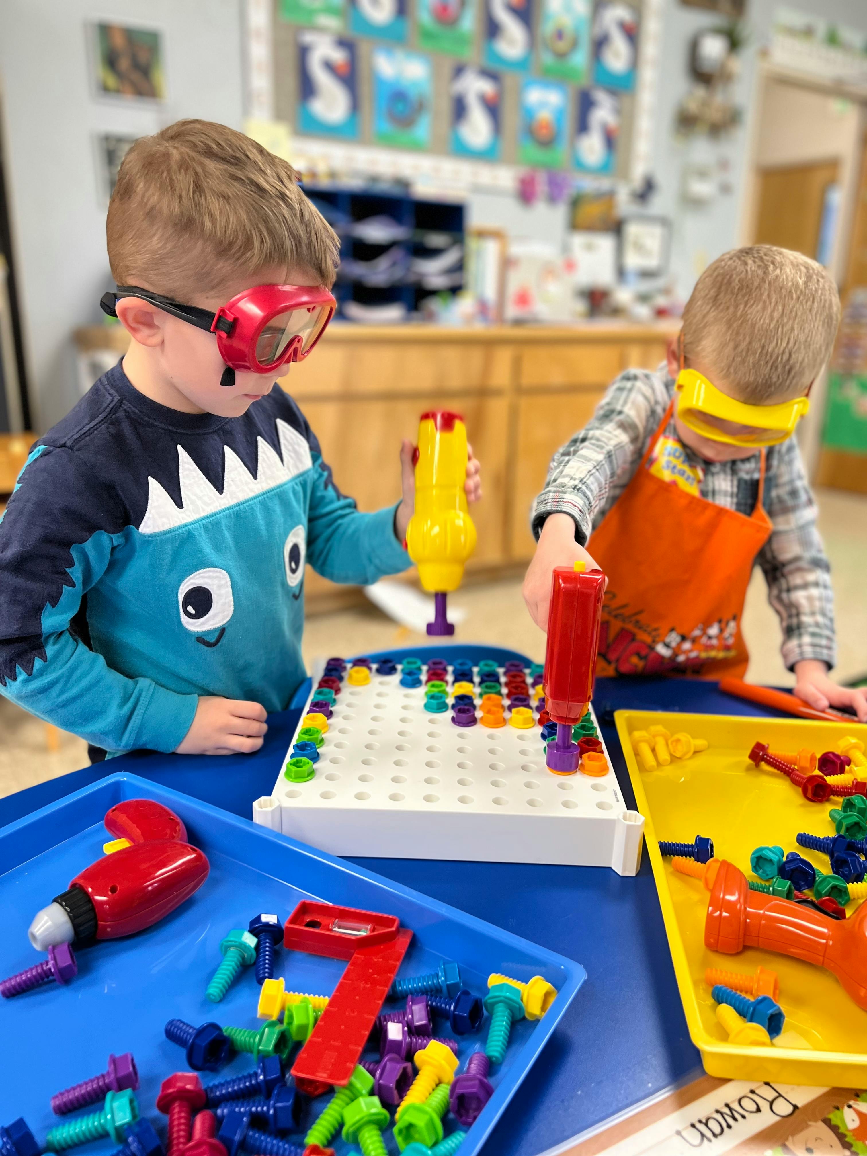 Two children wearing safety goggles playing with toy drills and pegboards