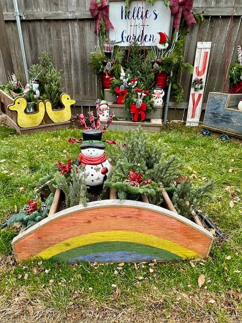 Outdoor holiday decorations with a snowman, evergreen plants, and a rainbow